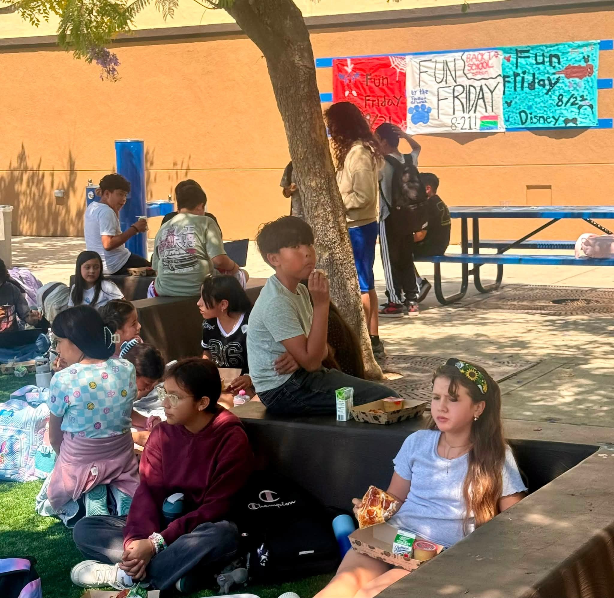 Students enjoy lunch in the shade near Fun Friday posters.
