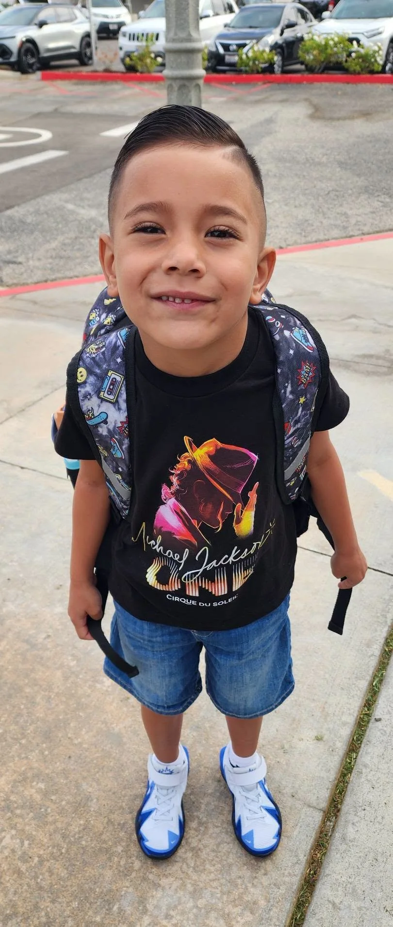 A young student with a backpack smiles outside the school.