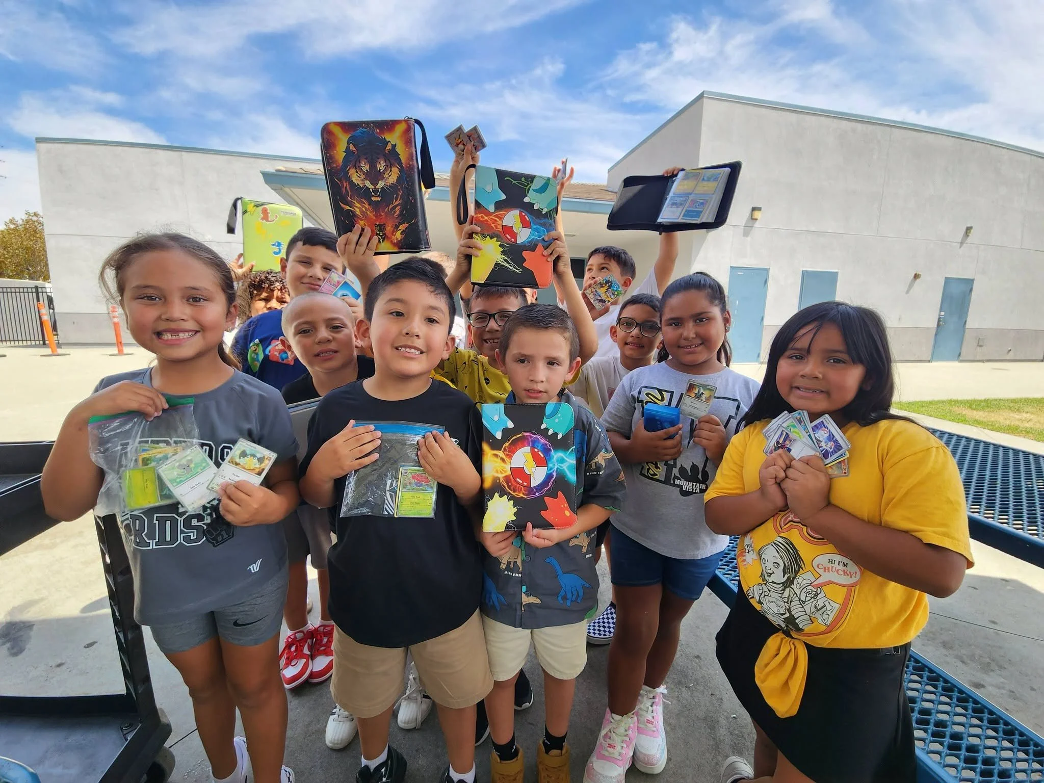 A group of Mountain Vista students proudly displays Pokémon cards and binders outdoors.