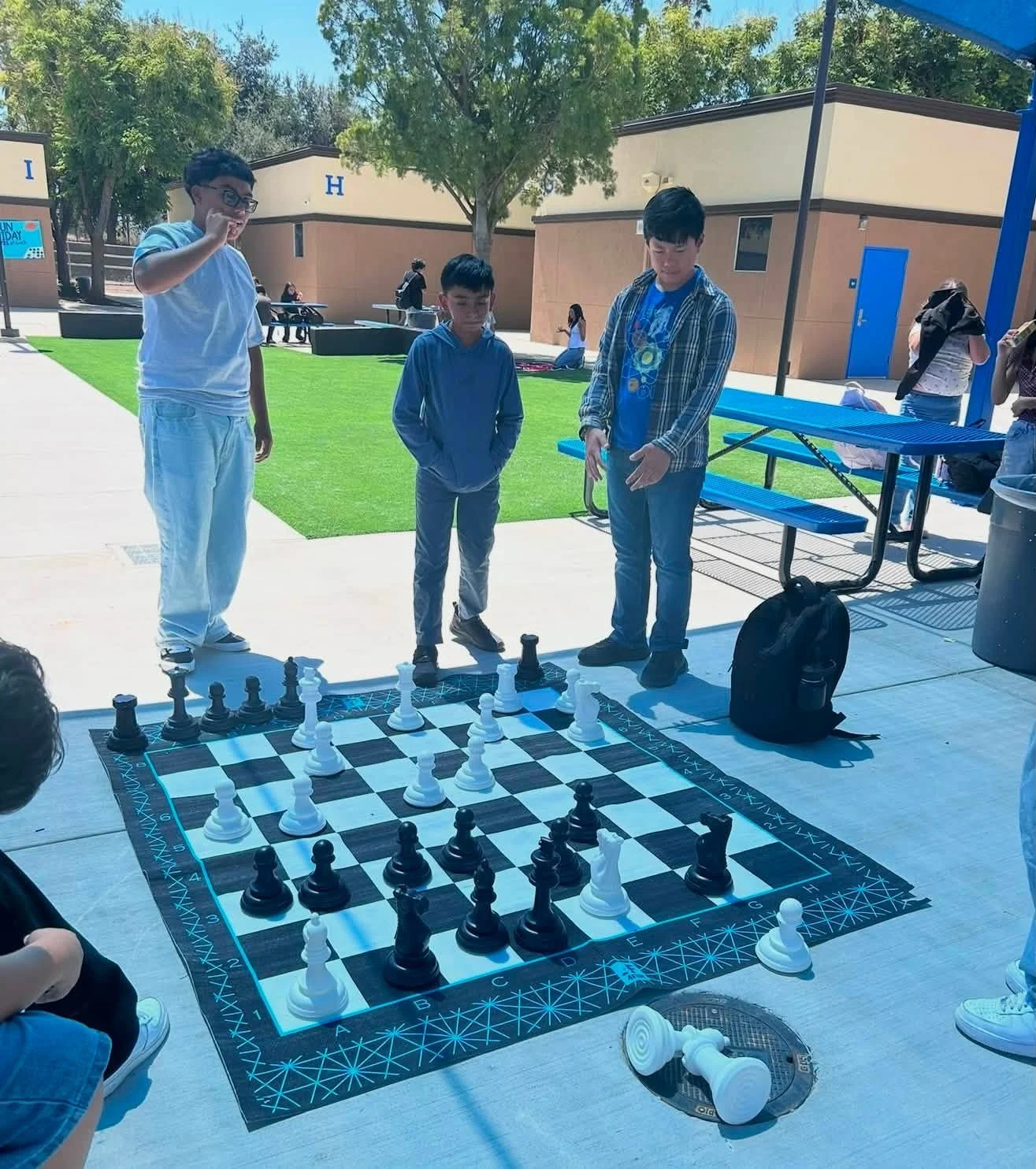 Students gather around an oversized outdoor chessboard.