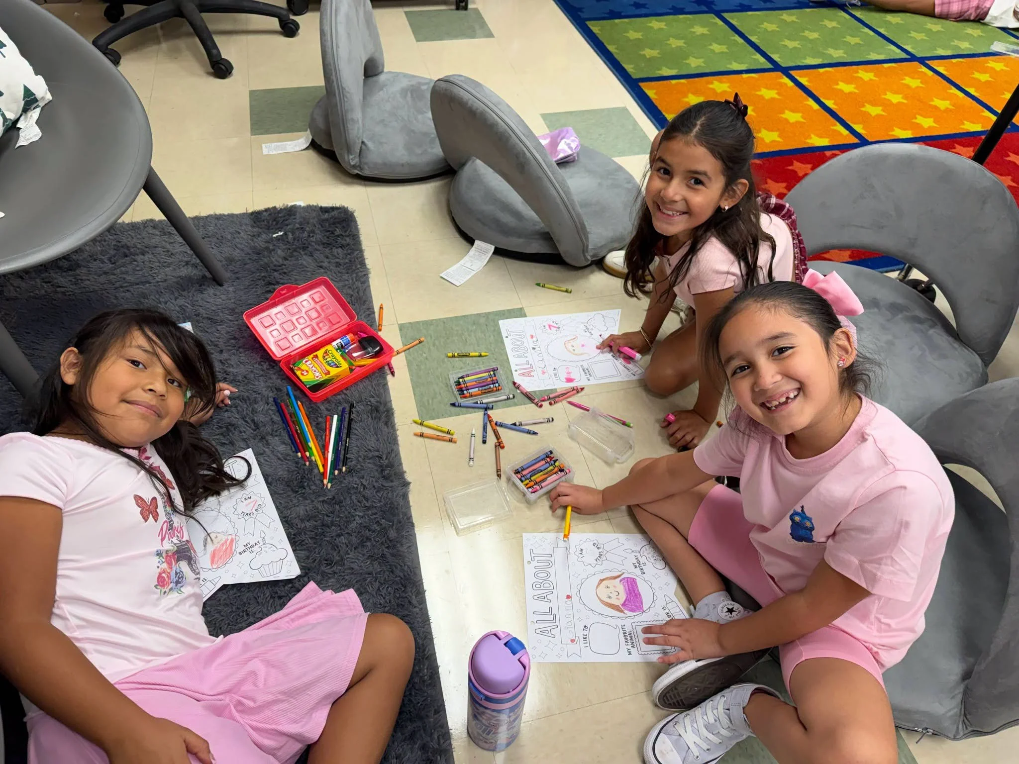 Students work on self-portrait worksheets while seated on the classroom floor.