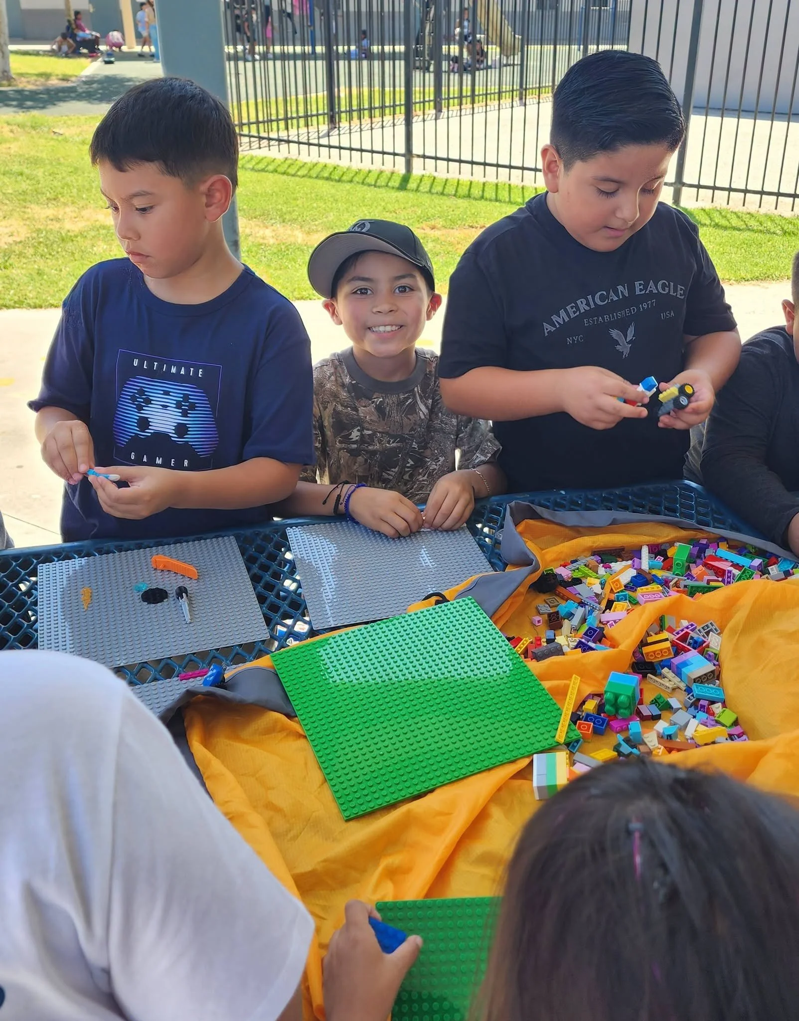 Students create Lego models together at a shaded picnic table.