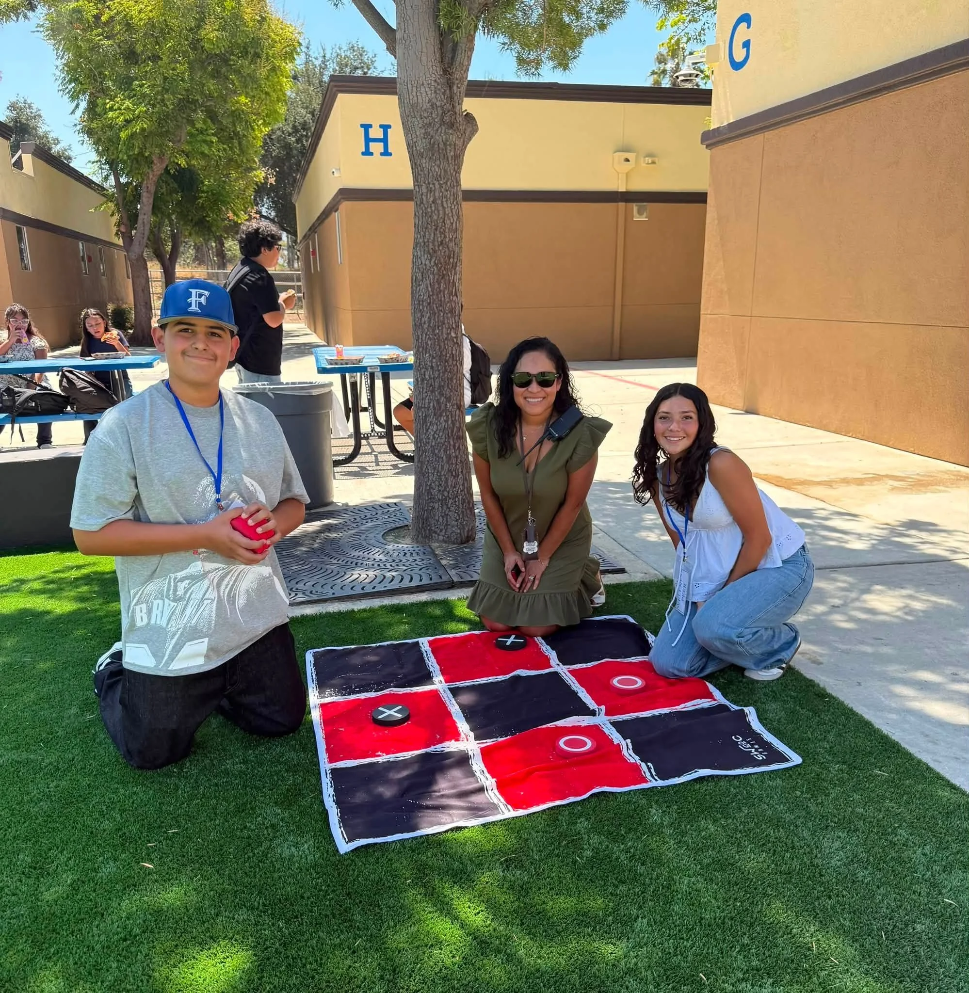 A student and two adults play oversized tic-tac-toe on the lawn.