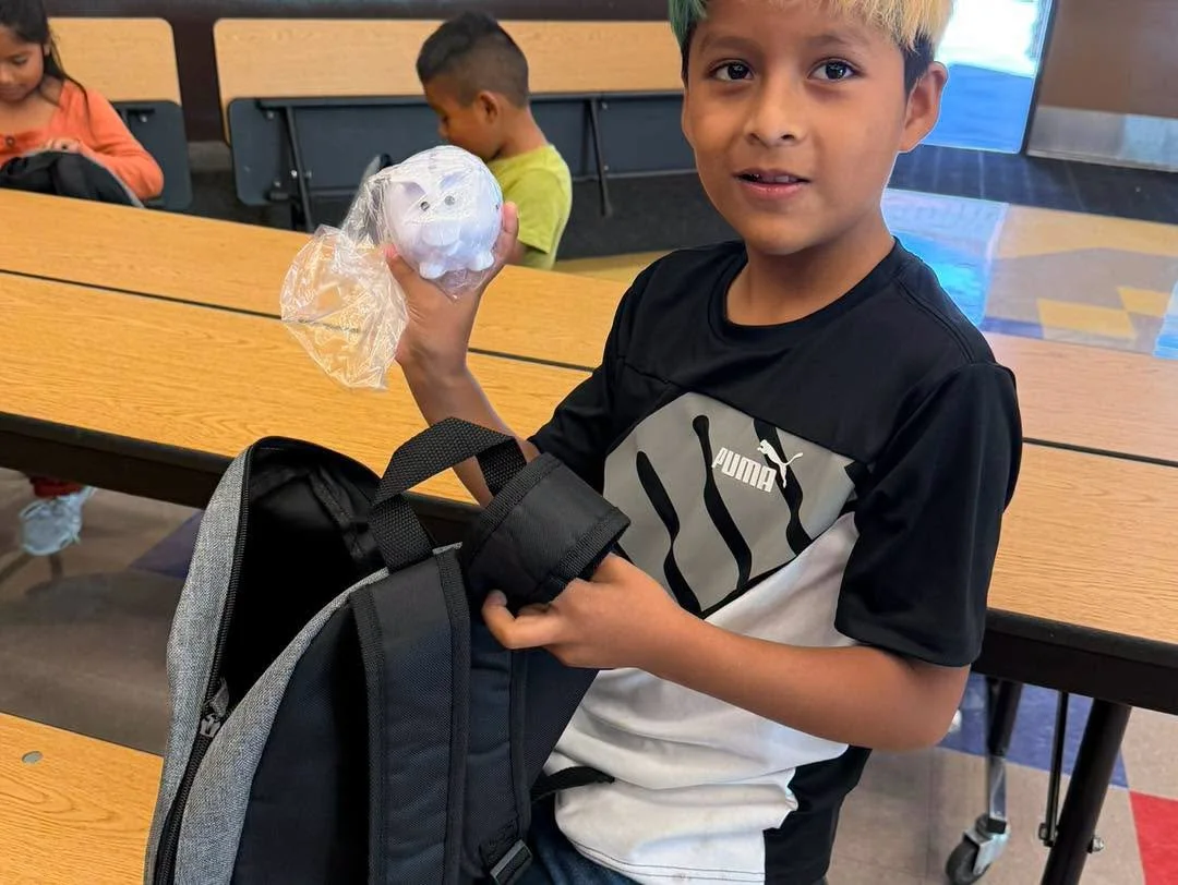 A student displays a donated piggy bank beside a new backpack.