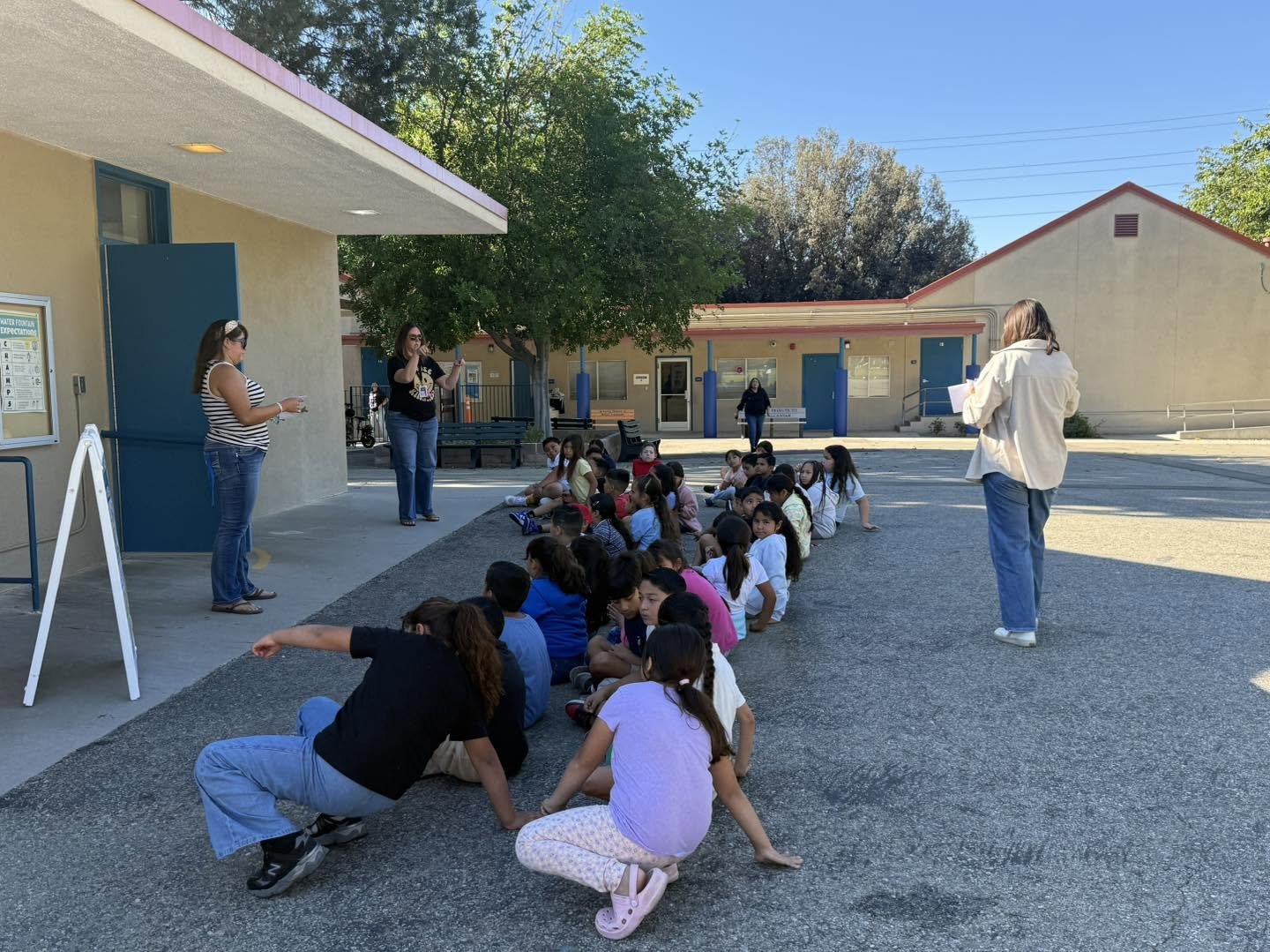 Staff review school expectations with students seated outside a building.