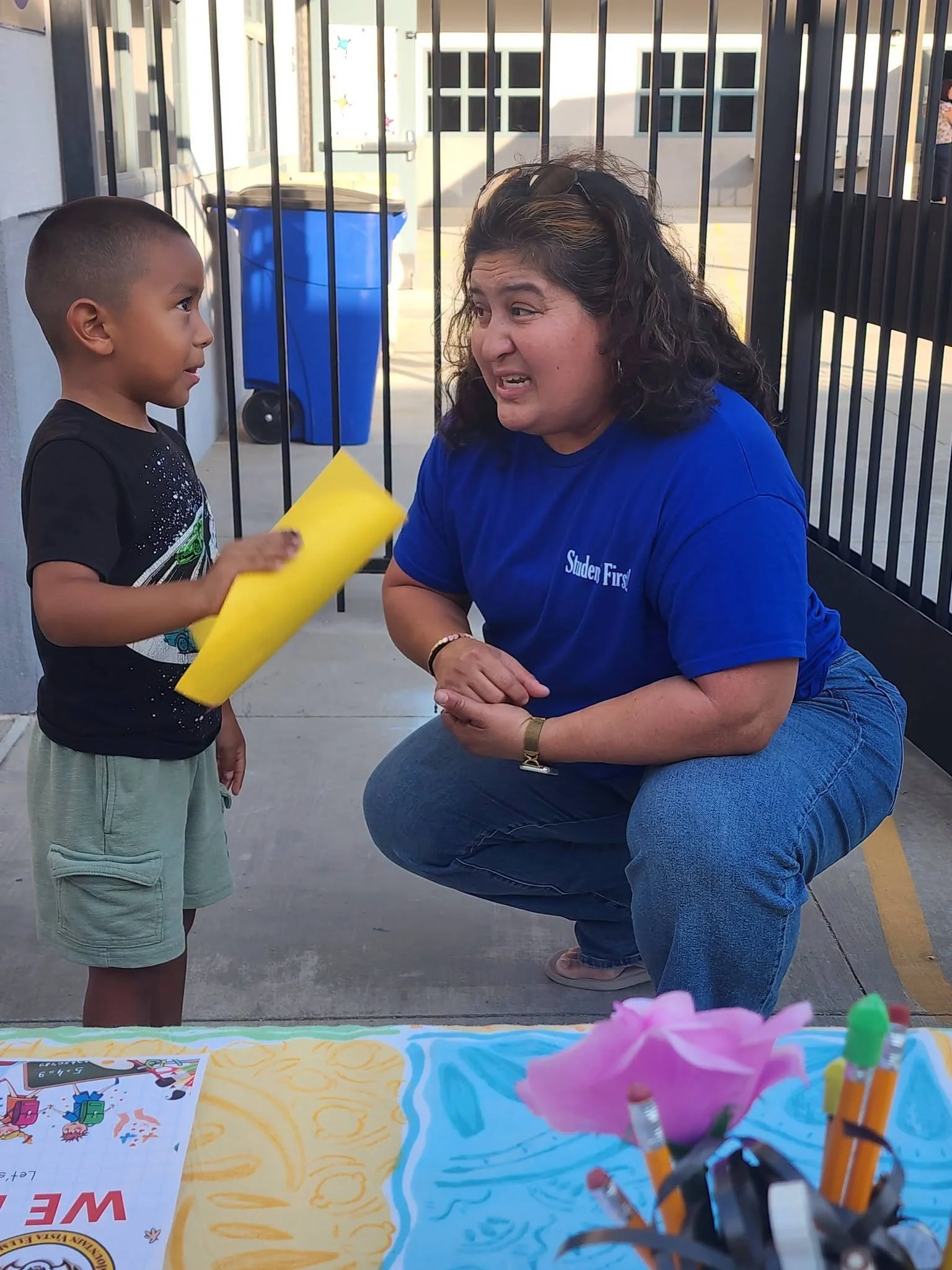 A staff member crouches to talk with a young student beside the welcome table.