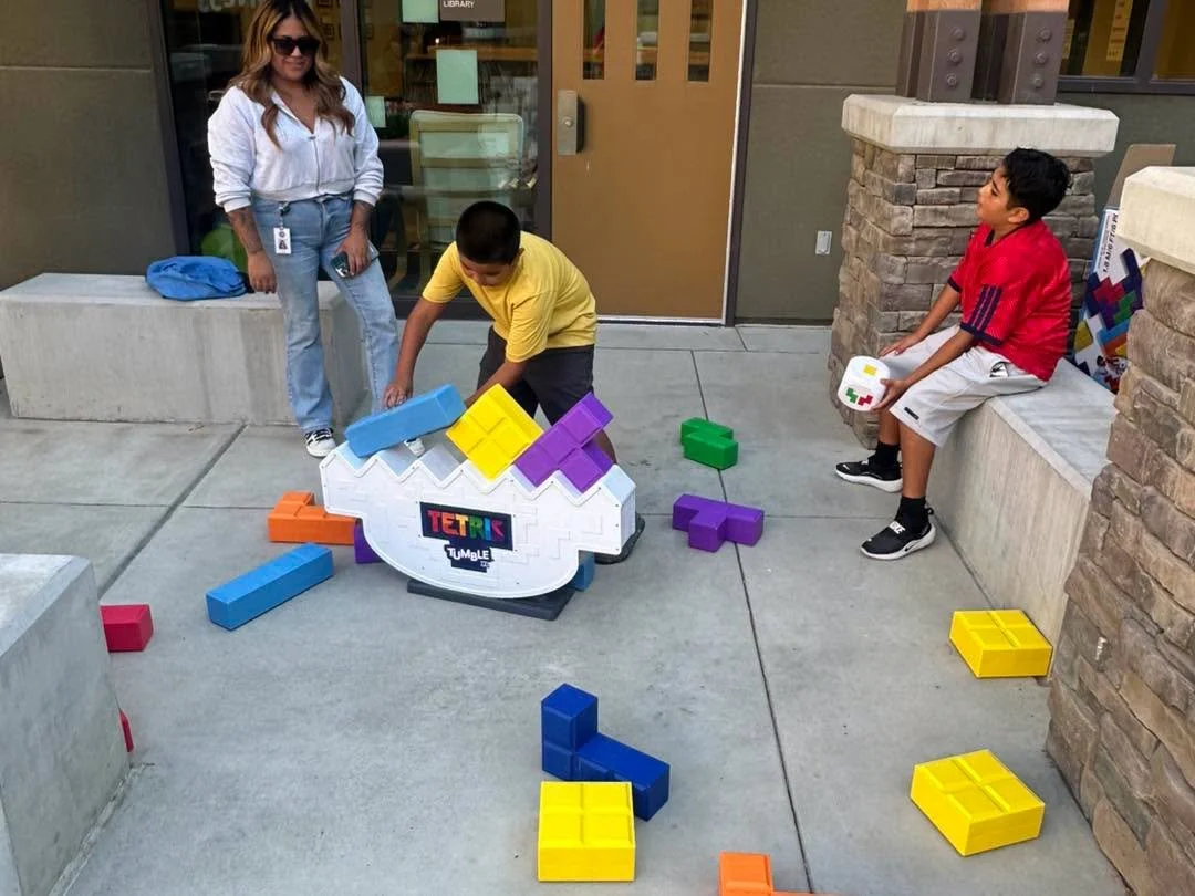 Children play a large Tetris balancing game outside.