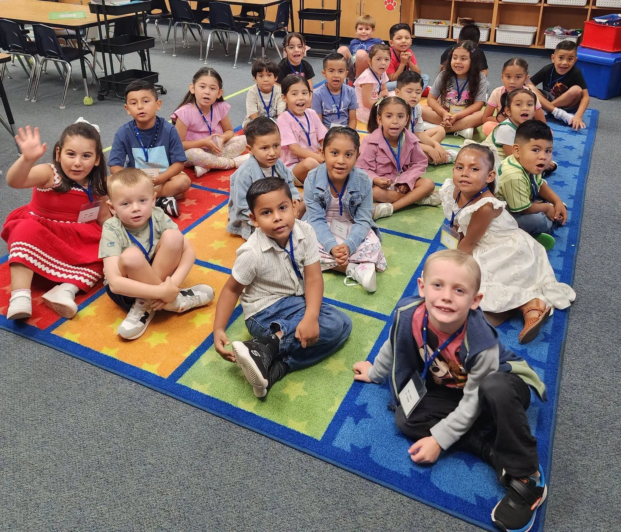 Students sit together on a colorful classroom rug on the first day.