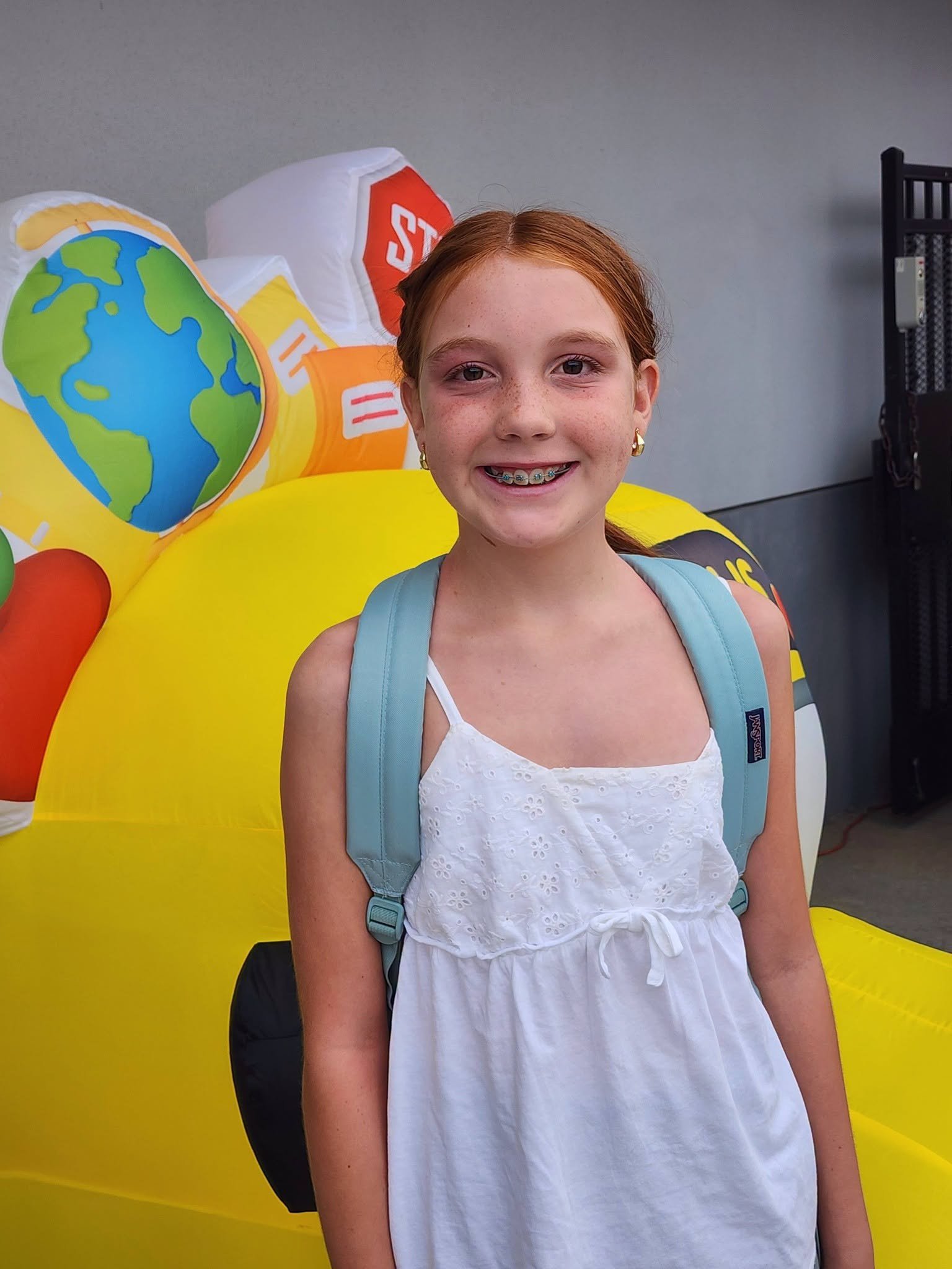 A smiling student with a backpack stands by the welcome decoration.