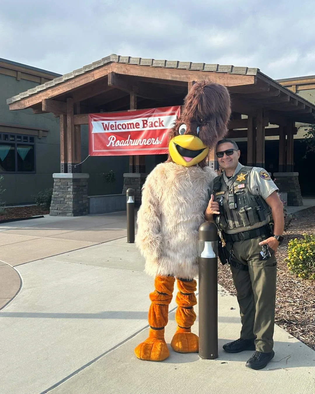 Ronnie the Roadrunner poses with a uniformed deputy outside school.