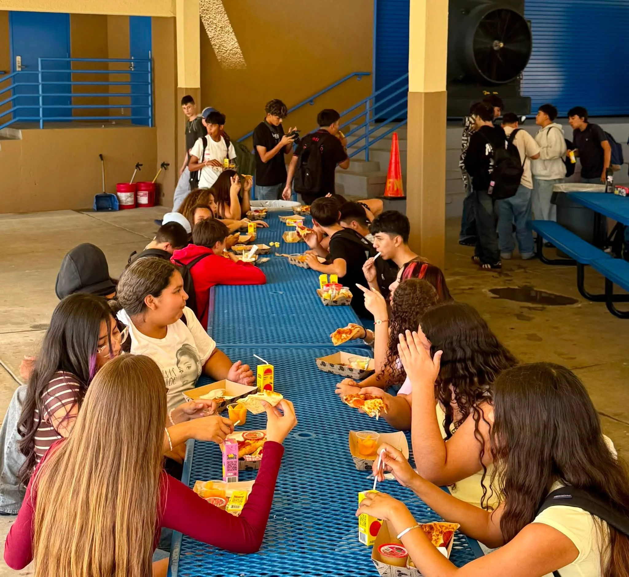 Students share lunch at a long blue picnic table.