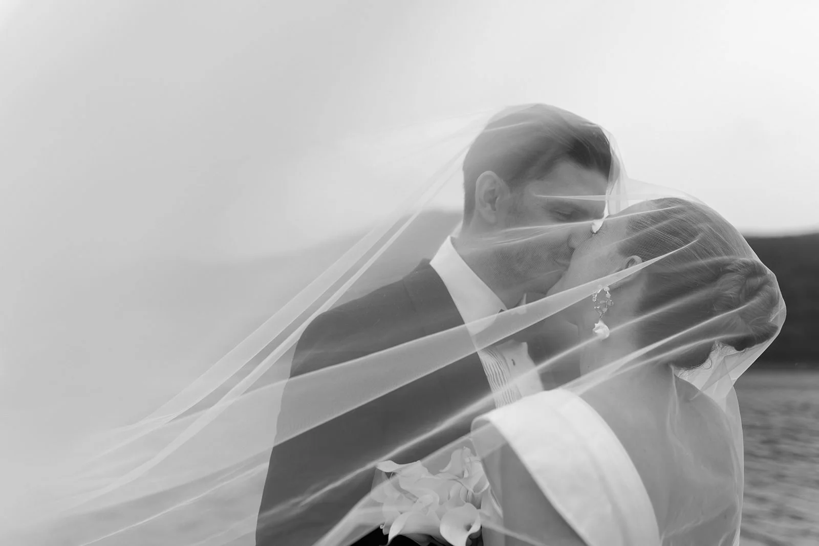 A black and white photo of a bride and groom kissing, partially covered by a veil.