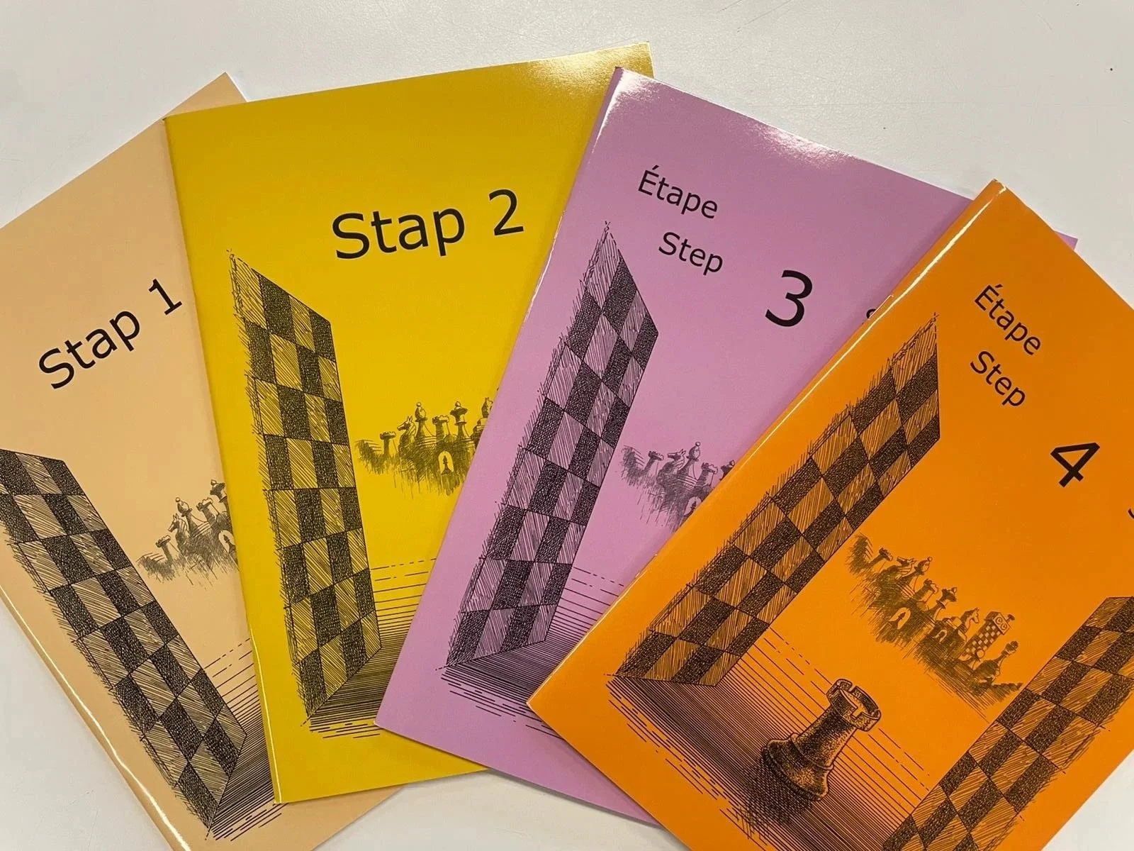 4 stappenboekjes van de stappenmethode om te leren schaken. De boekjes zijn beige, geel, paars en oranje met een voorkant met schaakstukken.