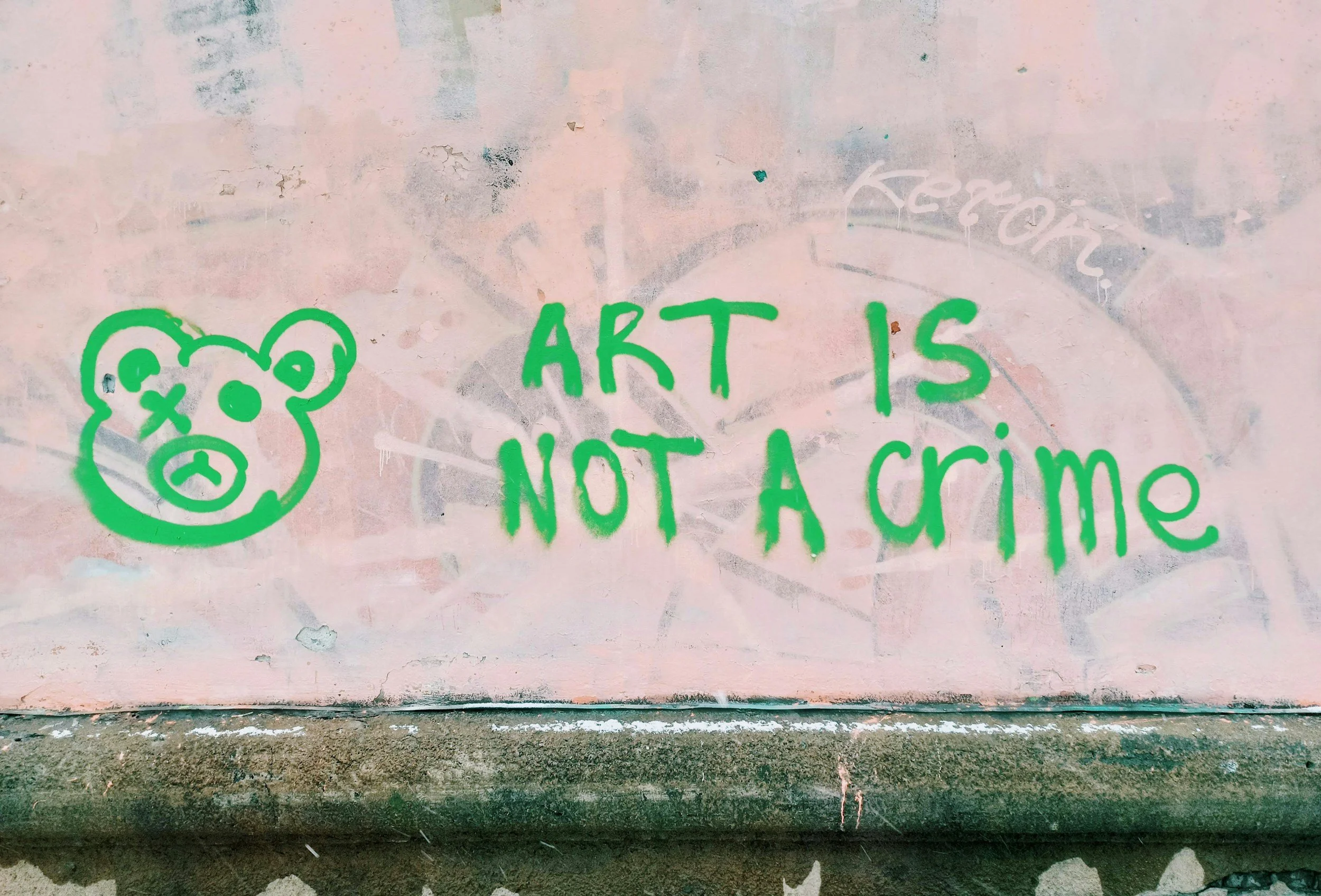 graffitti spray painted on a wall saying "art is not a crime" alongside a teddy bear face with one eye "x-ed" out
