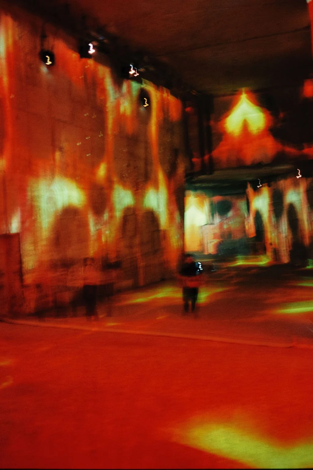 Colorful abstract light projection on a large wall with some silhouettes of people in a dark indoor setting.