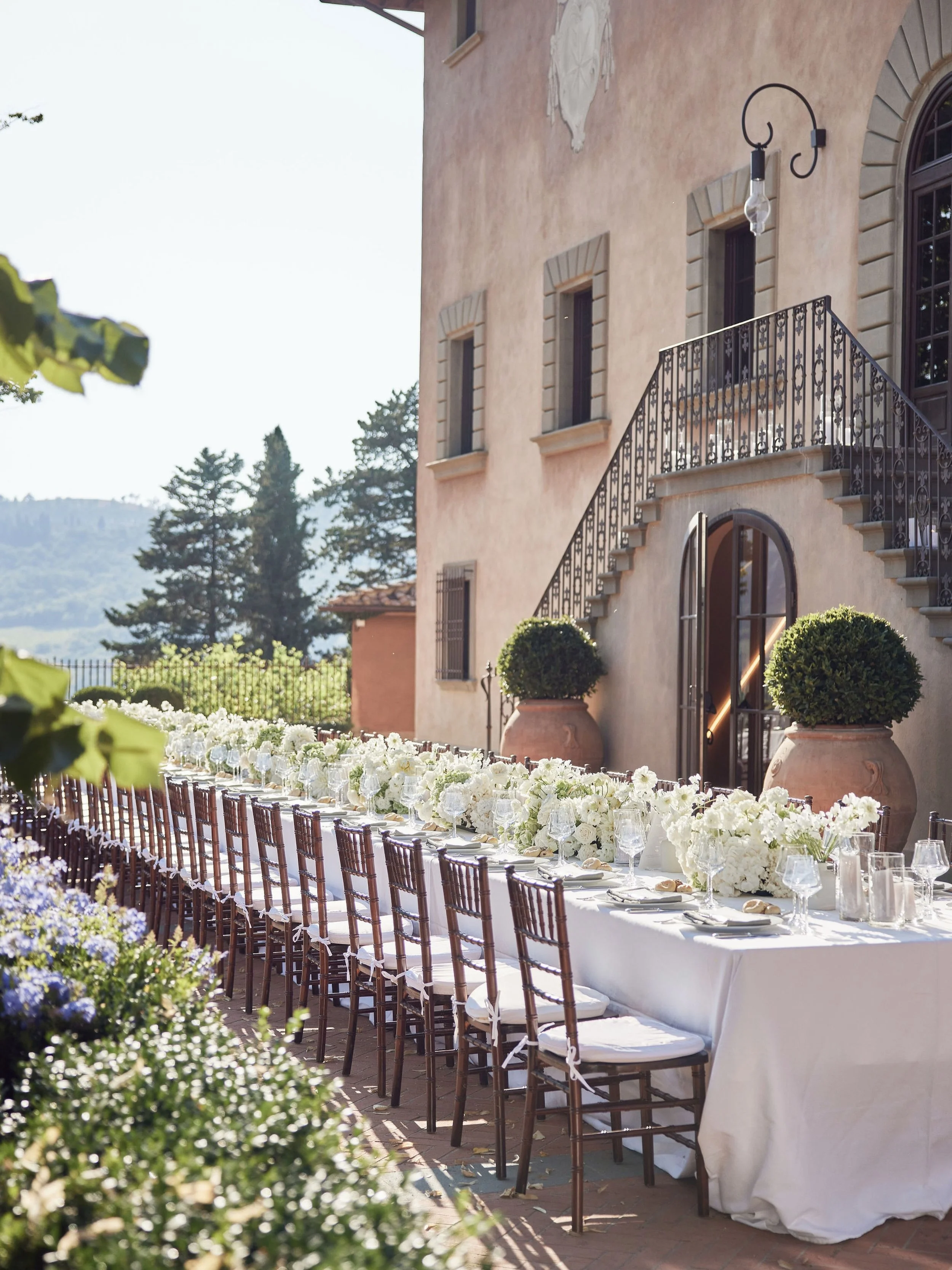 Dinner in the Tuscan countryside, just as the light begins to leave the day. 

At Vignamaggio, guests gathered along the fa&ccedil;ade of the villa for a table dressed in layers of white, softened by flowers and candlelight against centuries-old ston