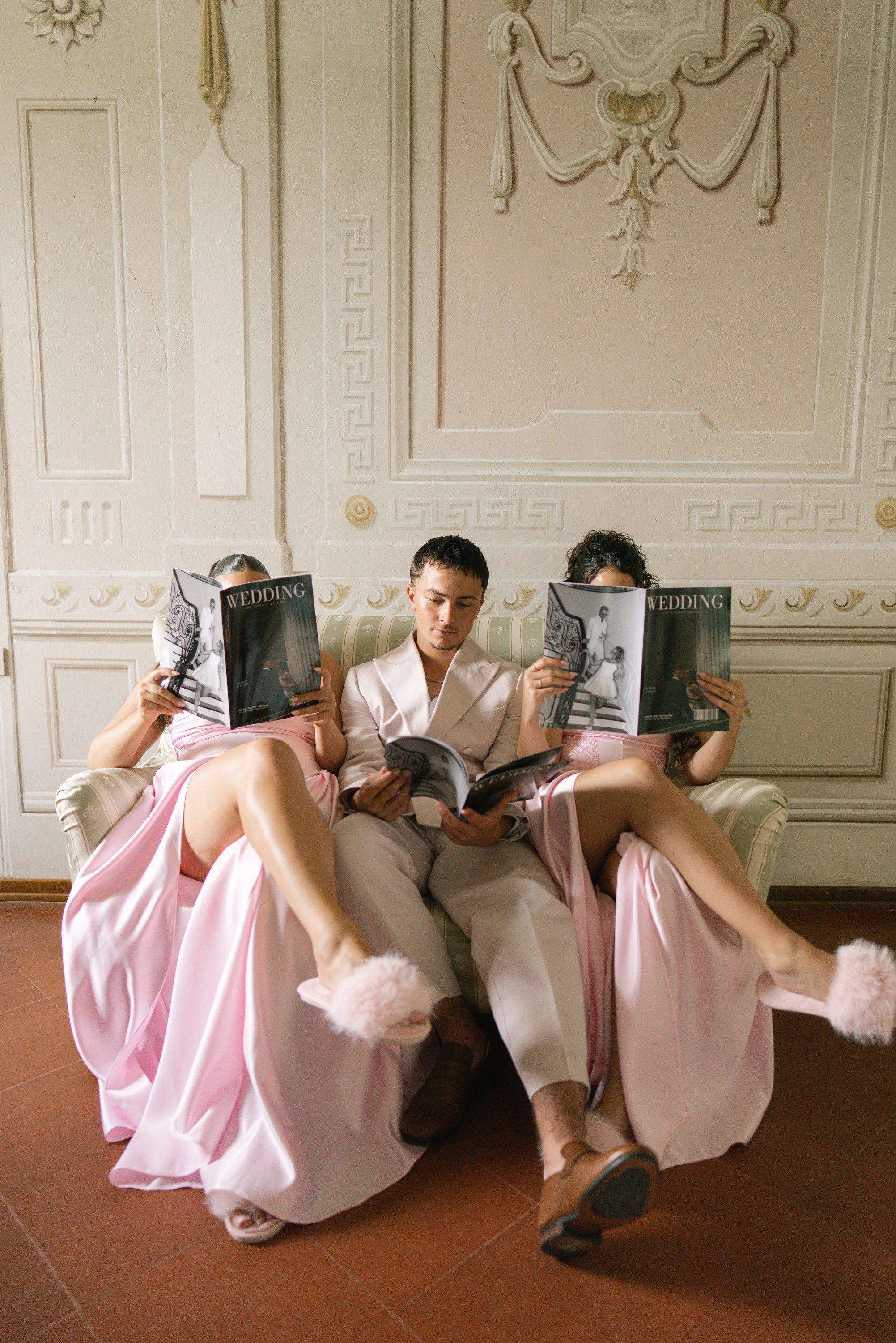 A wedding party reading magazines together in an ornate room.
