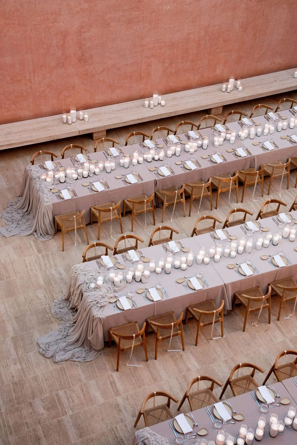 Candlelit wedding tables viewed from above in a pink courtyard.
