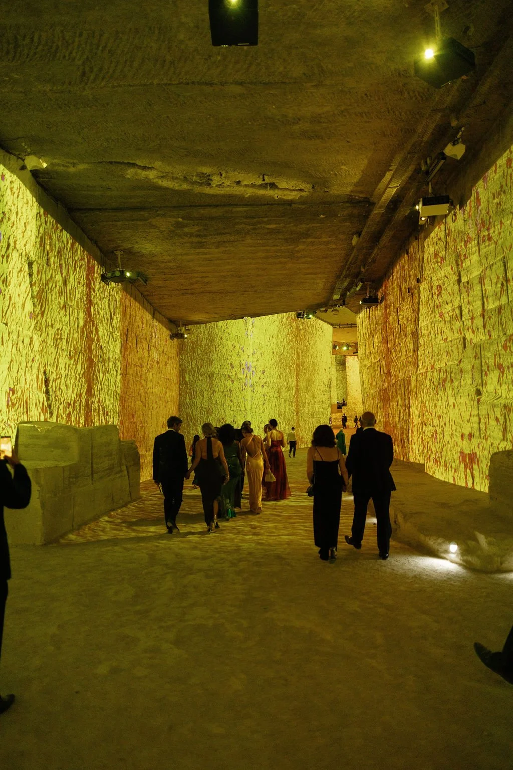 People walking through an underground tunnel with walls illuminated by colorful light projections.