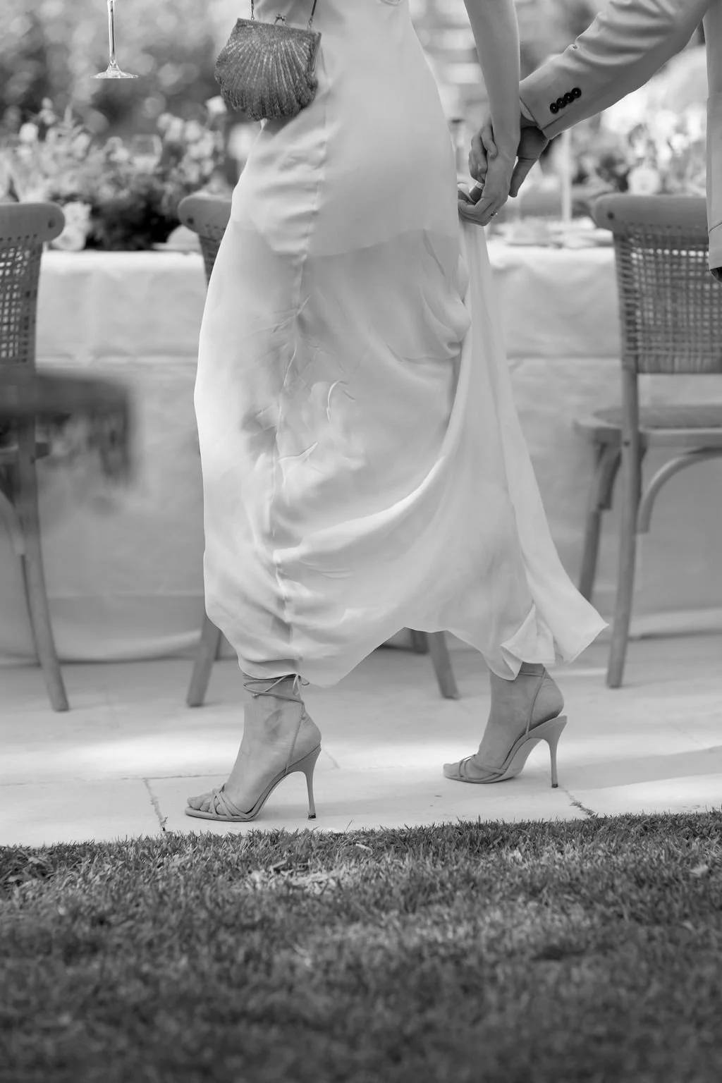 A bride in a wedding dress and high heels holding hands with a groom in a suit during their wedding reception.
