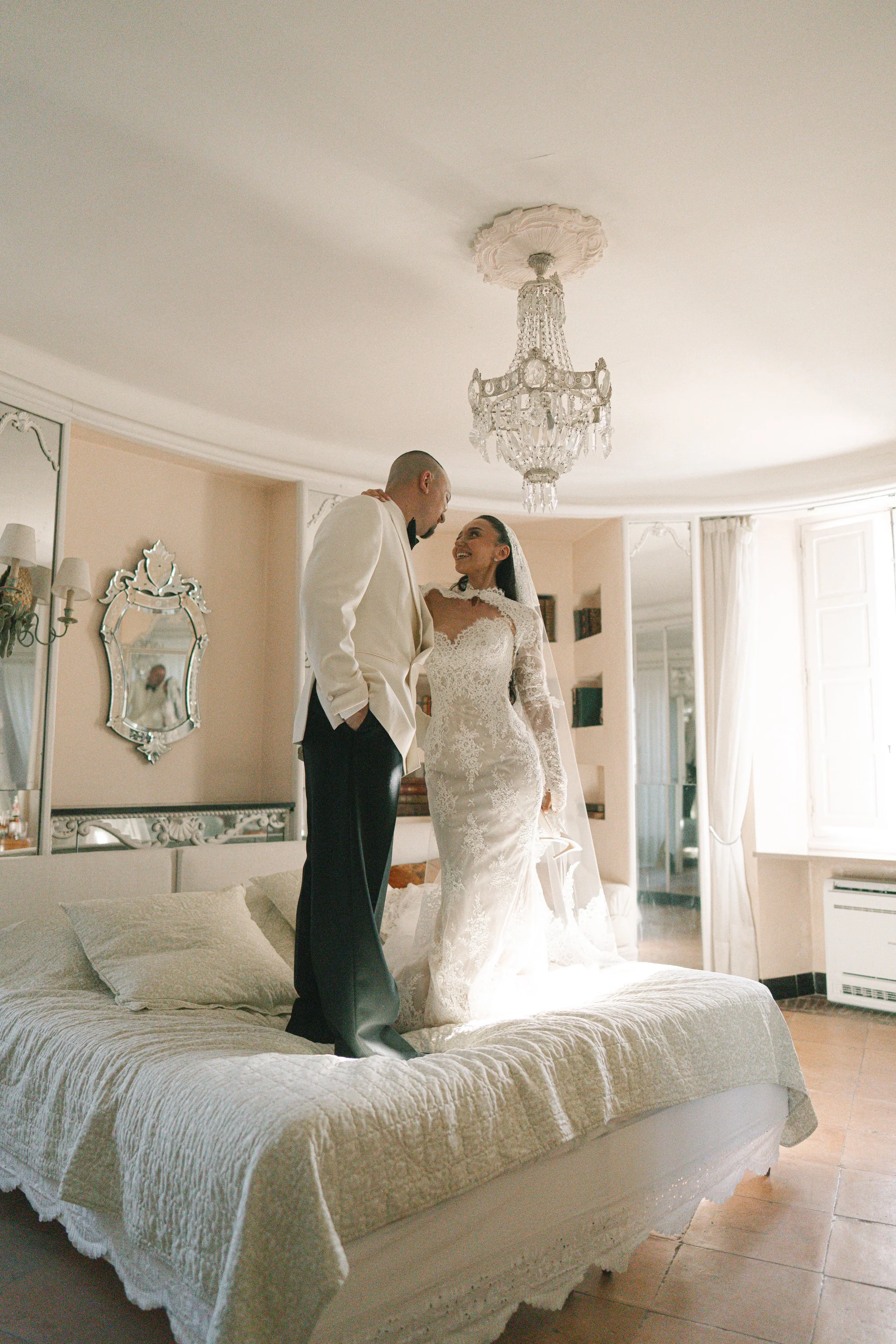 Newlyweds standing together on a bed in a bright elegant room.