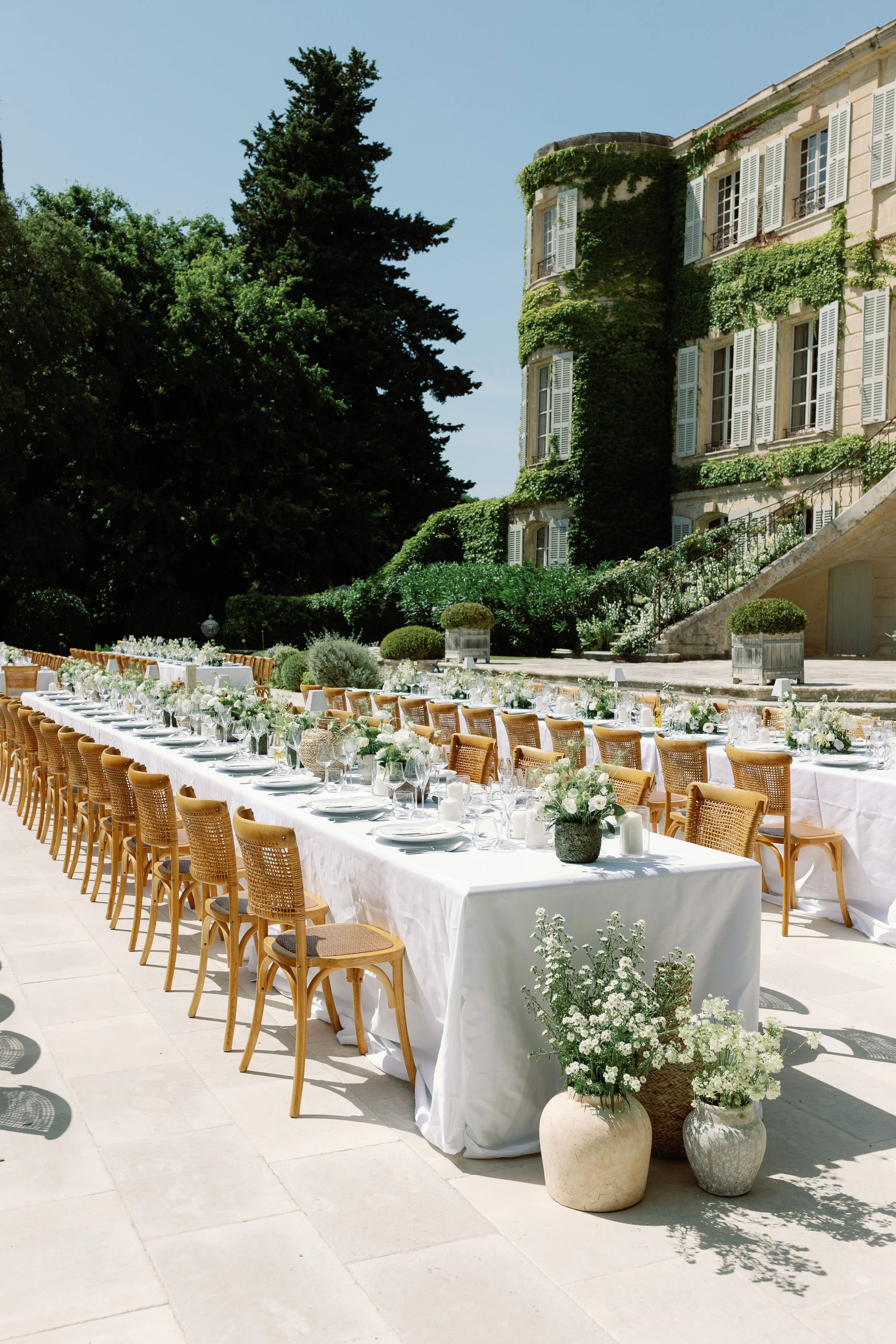 White wedding tables and woven chairs outside an ivy-covered chateau.