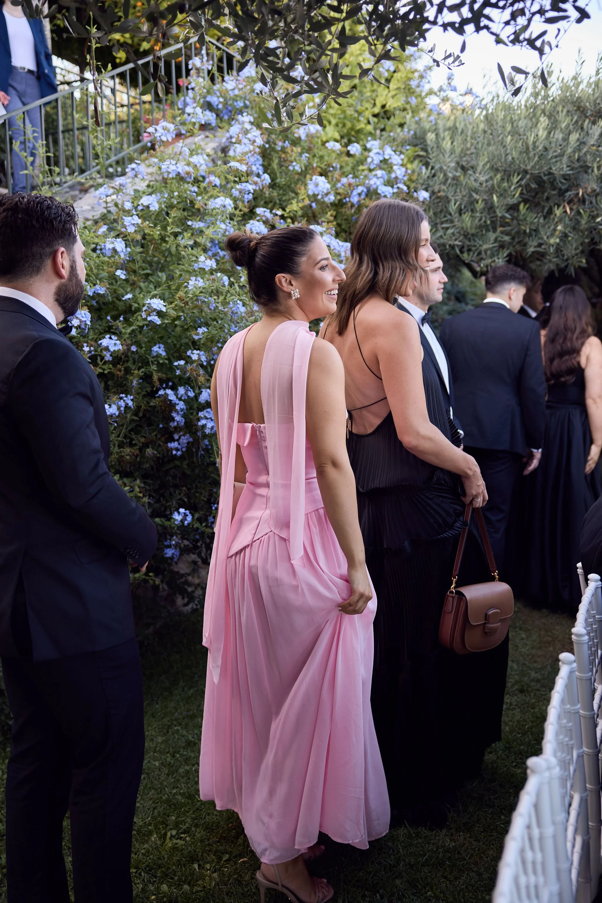 People dressed in formal attire attending an outdoor event with lush greenery and blooming flowers.