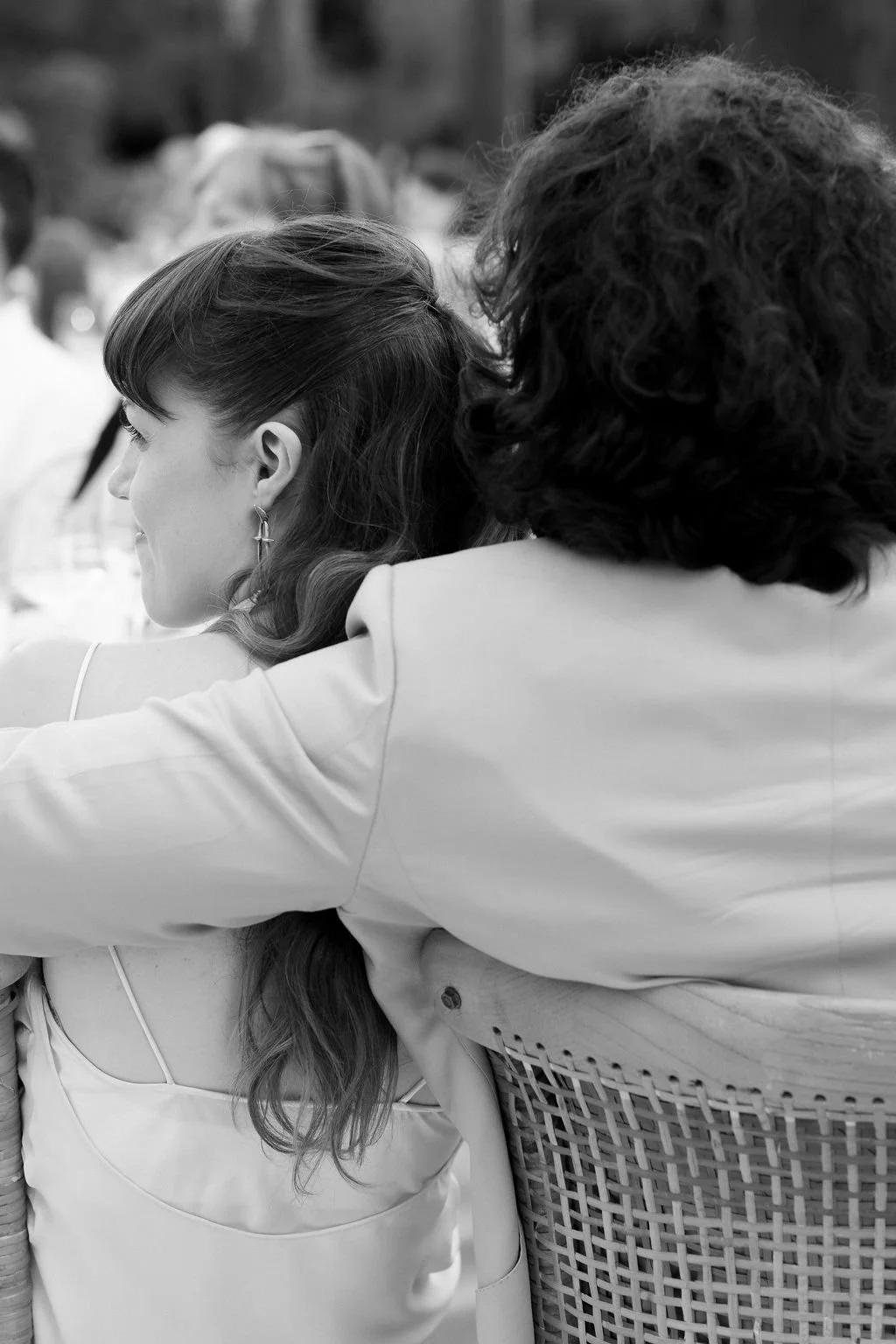 Black and white photo of a woman and a man sitting close together at an outdoor event, with the woman smiling and the man's face turned away from the camera.