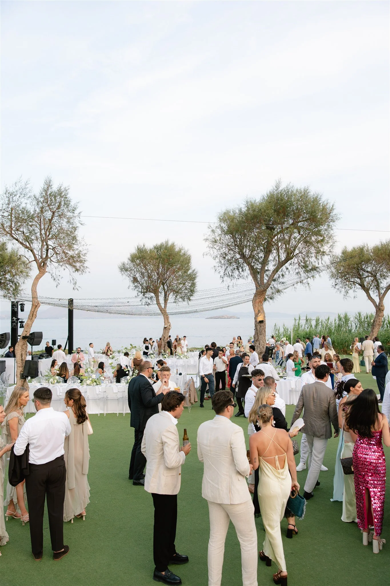 Guests in formal attire gathering beside the water for an outdoor celebration.