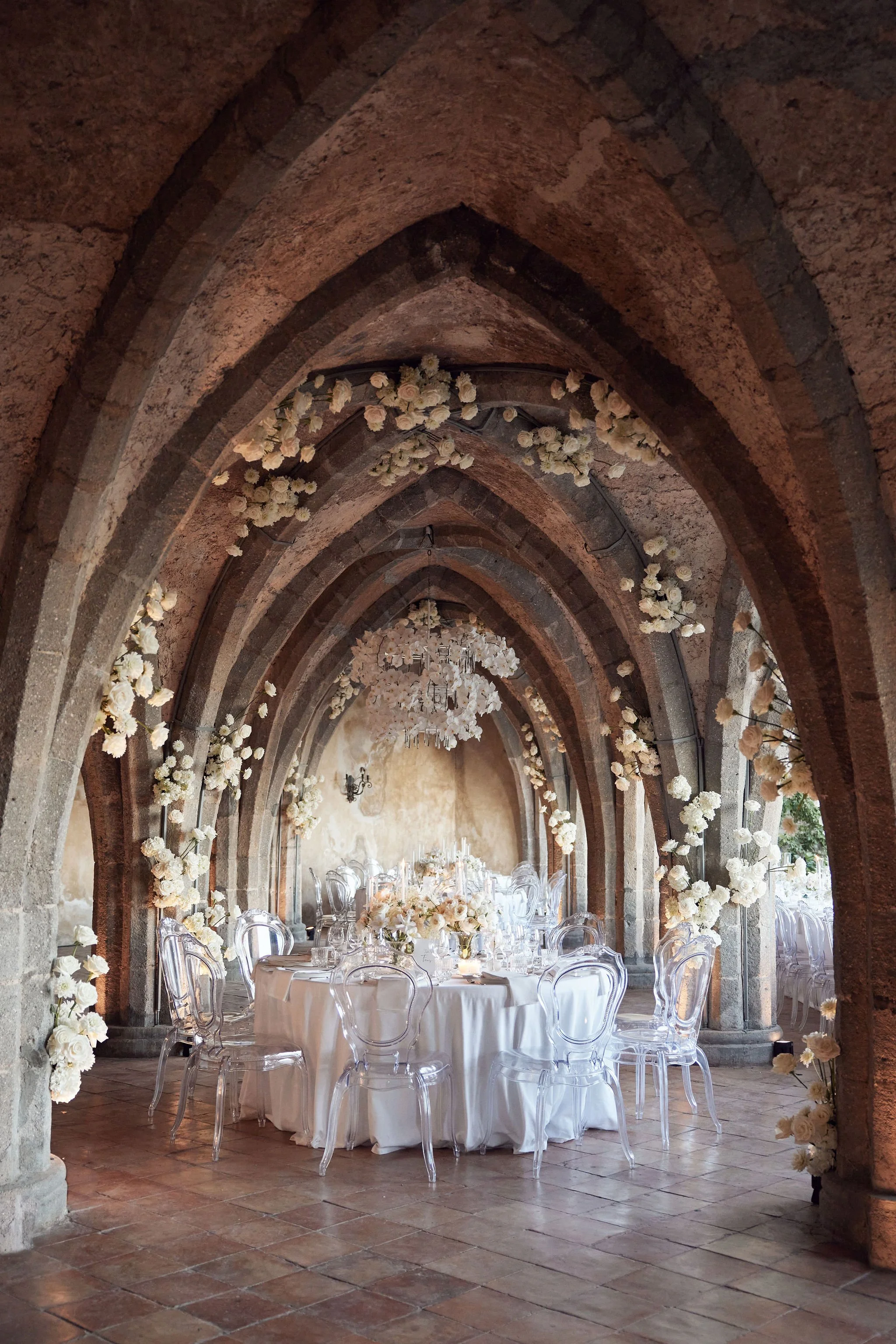 Round wedding tables beneath vaulted stone arches.