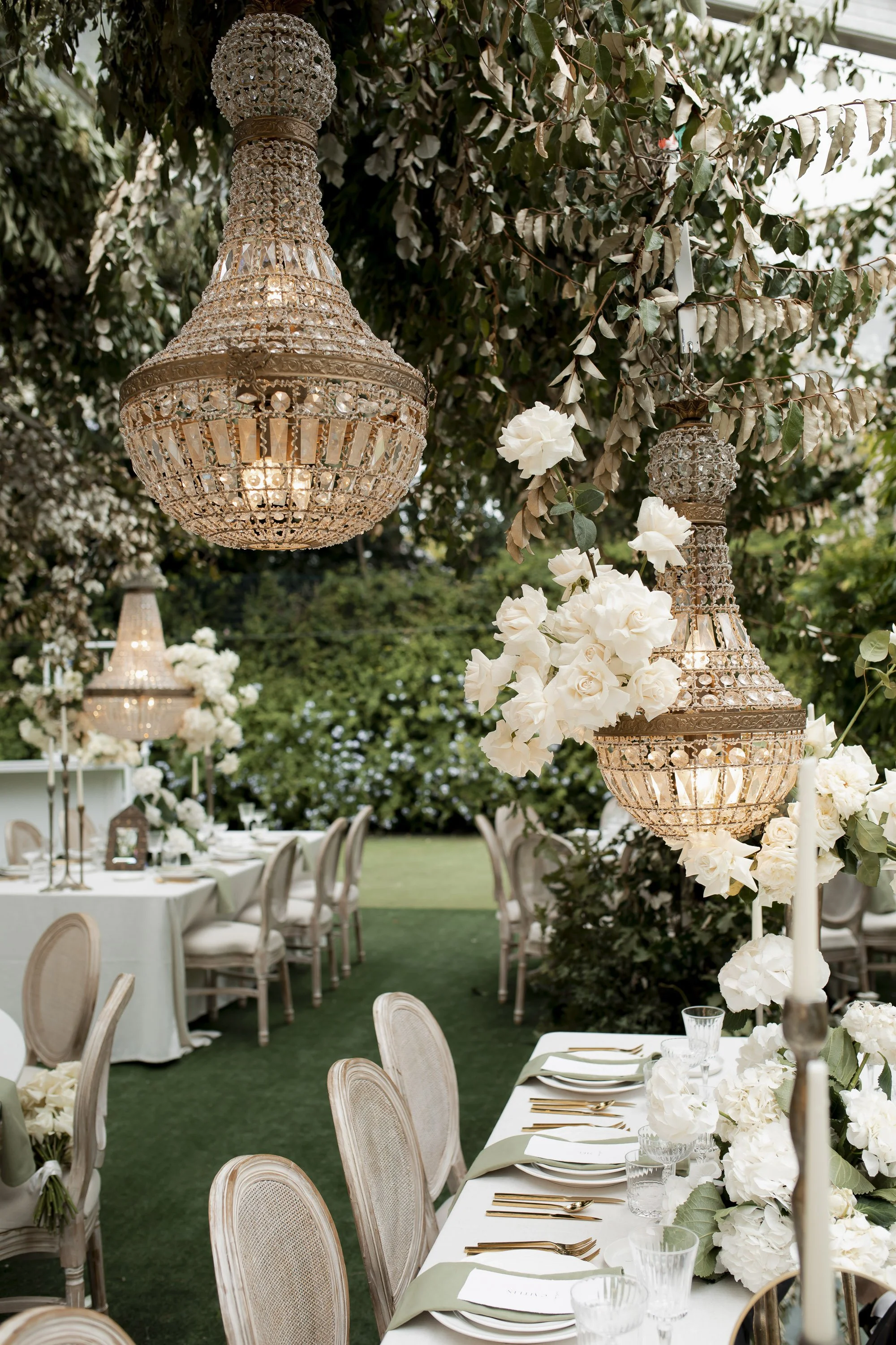 Crystal chandeliers and white flowers above garden reception tables.