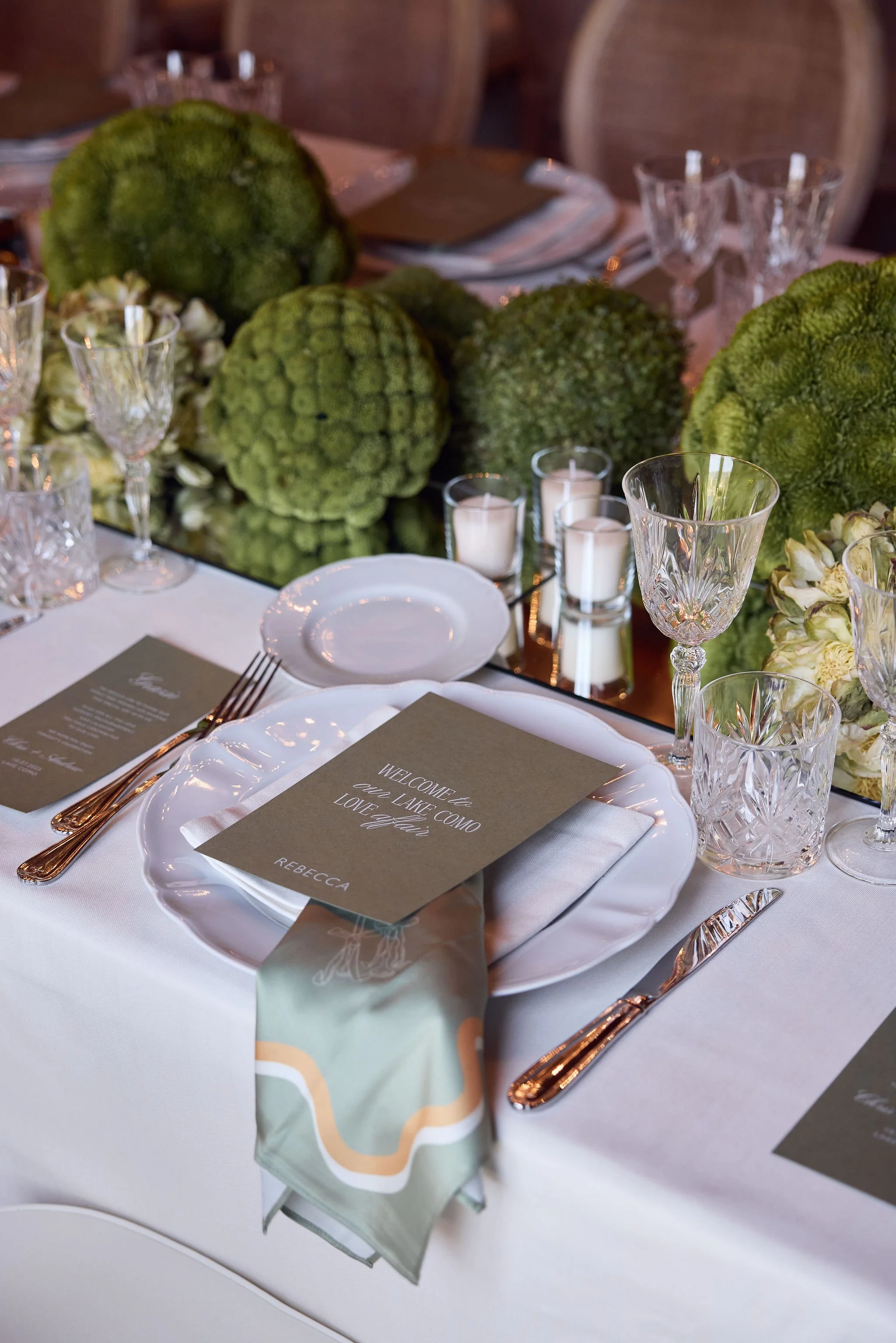 Green floral arrangements and crystal glassware at a wedding table.