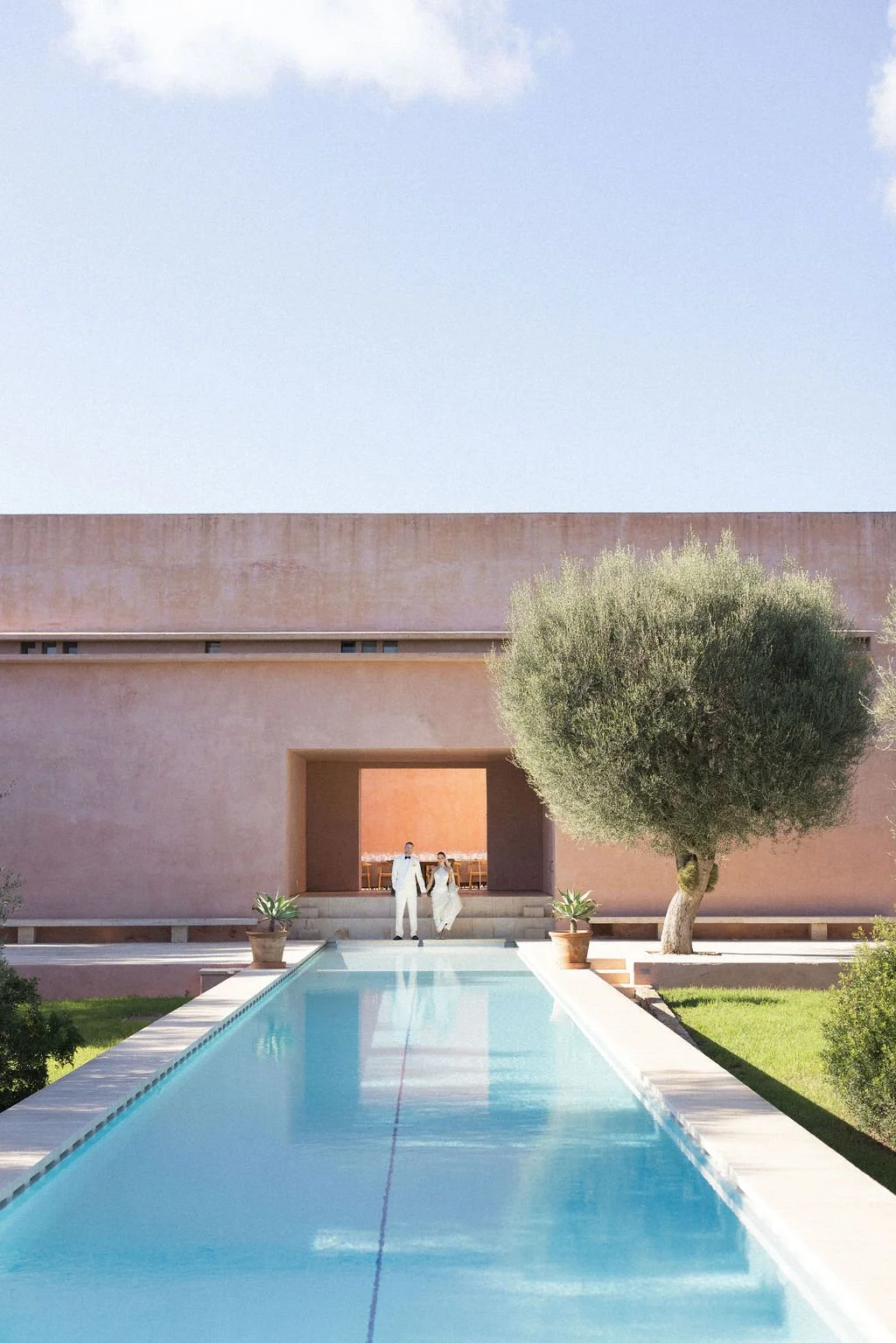 A couple beside a swimming pool at a pink modern villa.