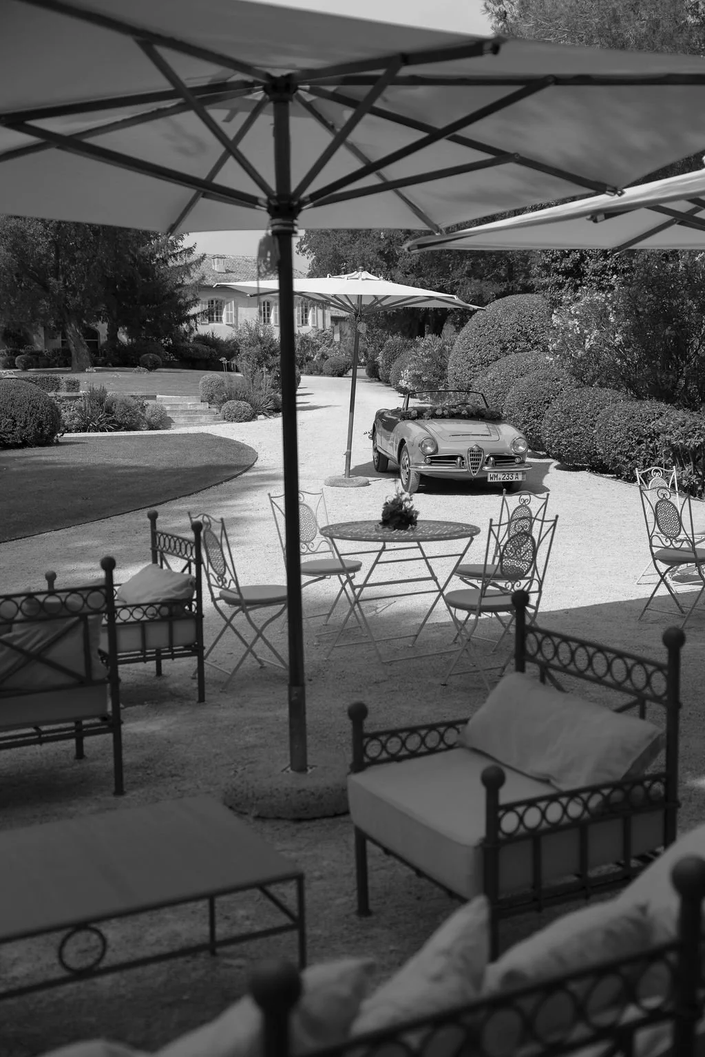 Outdoor garden patio with iron furniture, large umbrella, and a vintage convertible car in the background