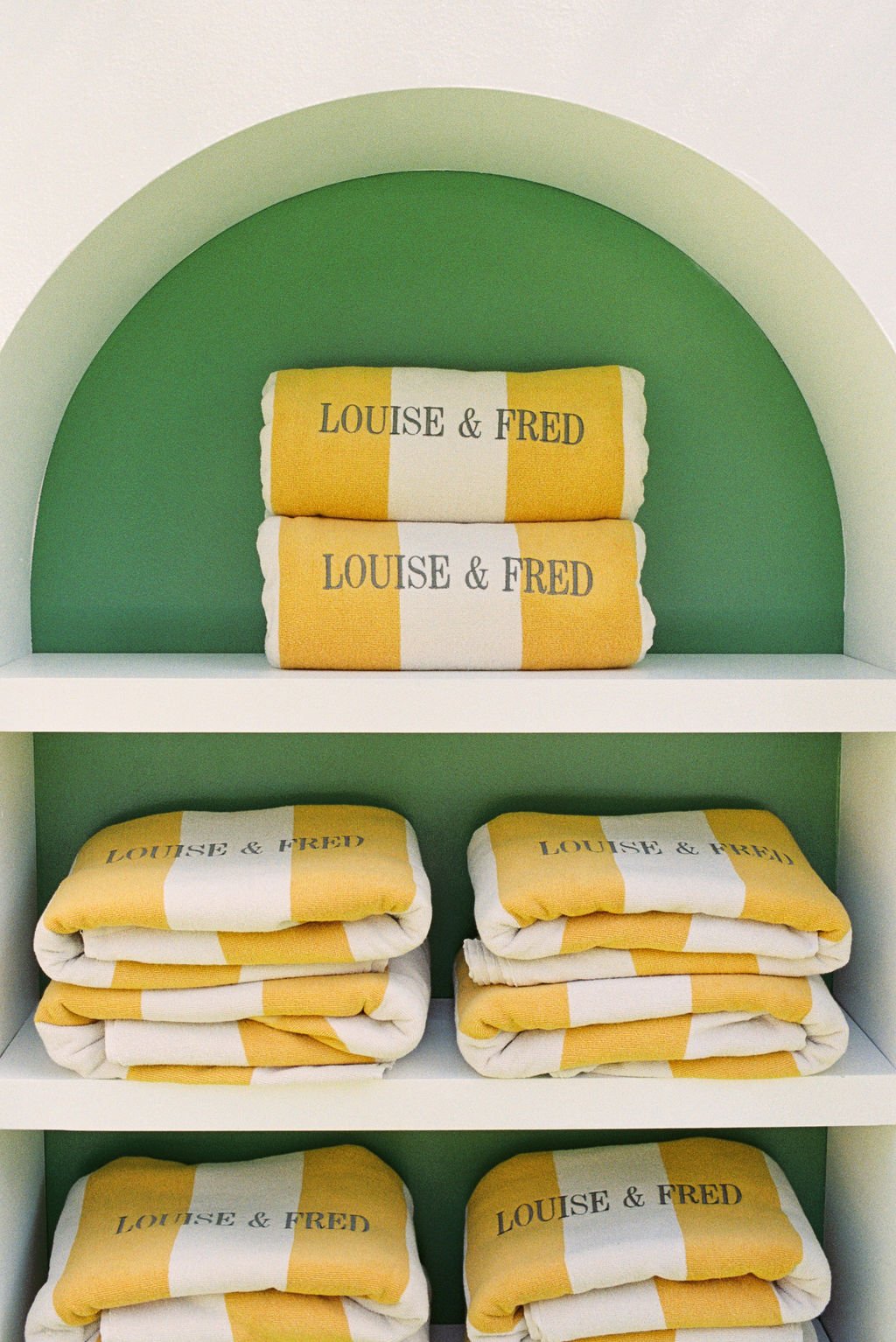 Display shelf with neatly folded yellow and white striped towels with the words 'LOUISE & FRED' printed on them.