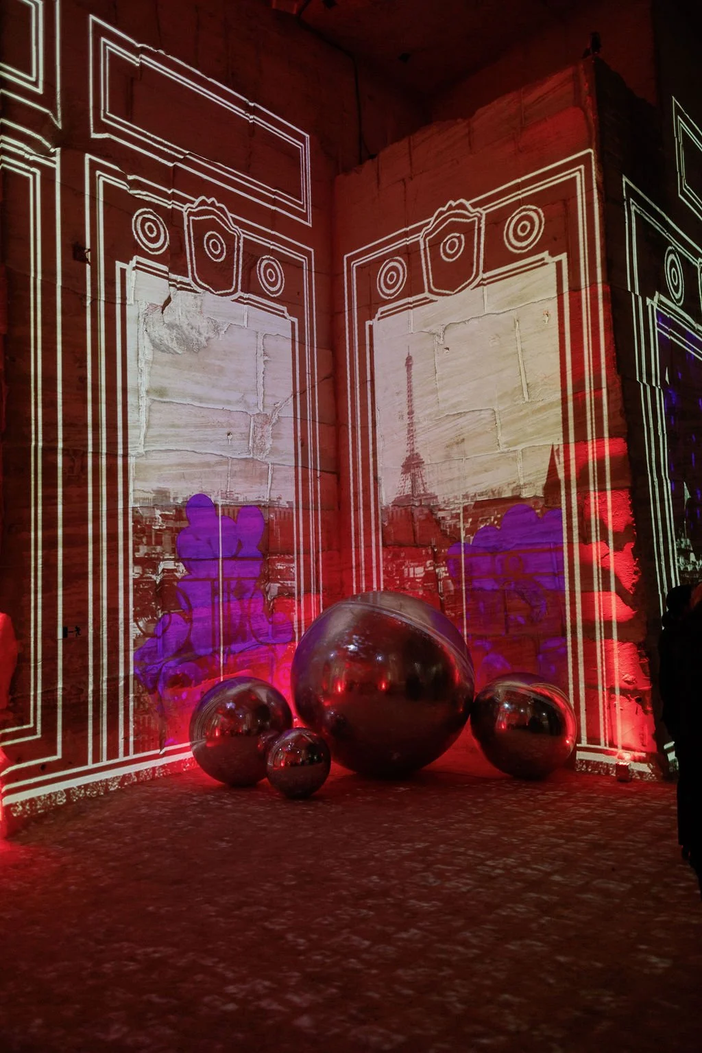 Light projection of architectural line art on brick walls with the Eiffel Tower and purple graffiti, mirror balls on the ground reflecting the surroundings, red and purple lighting.