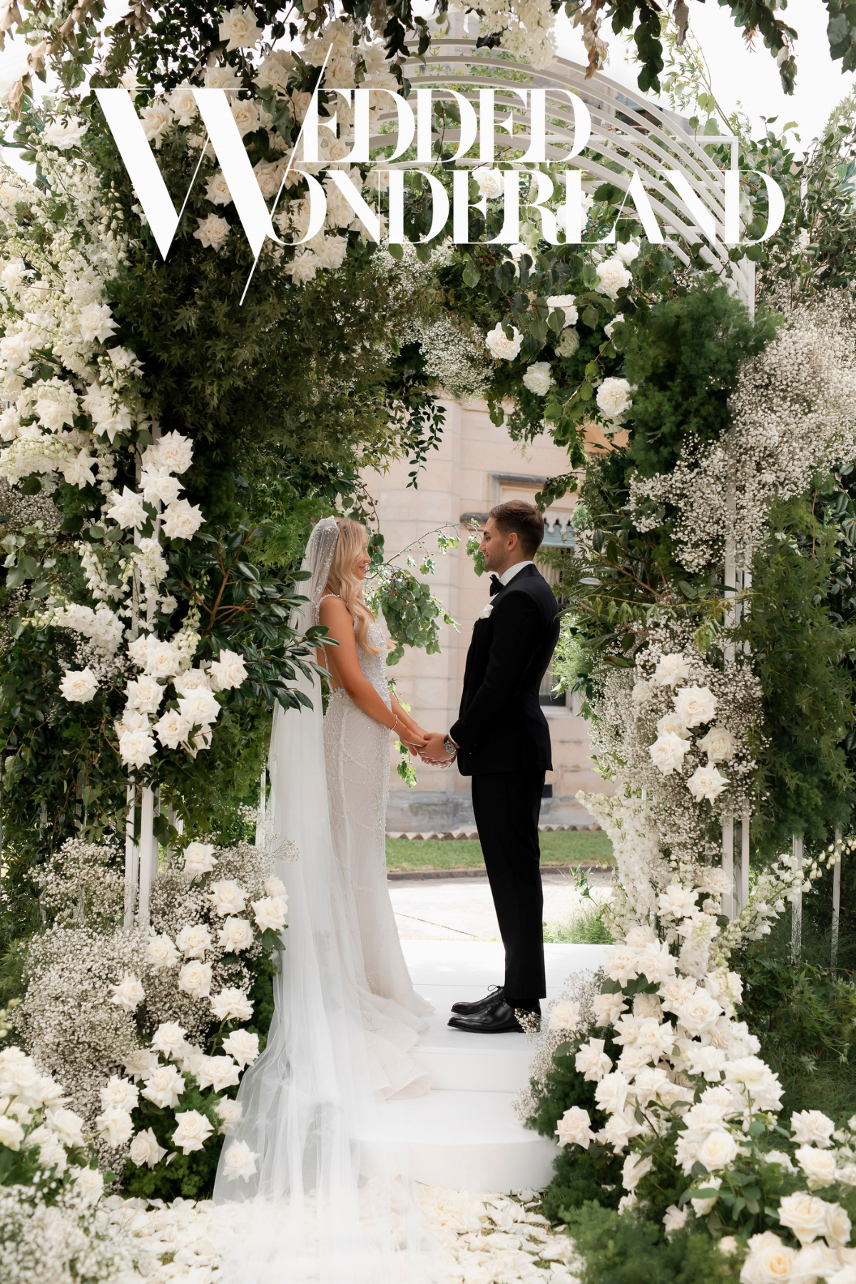 Wedded Wonderland — couple beneath a white floral wedding arch