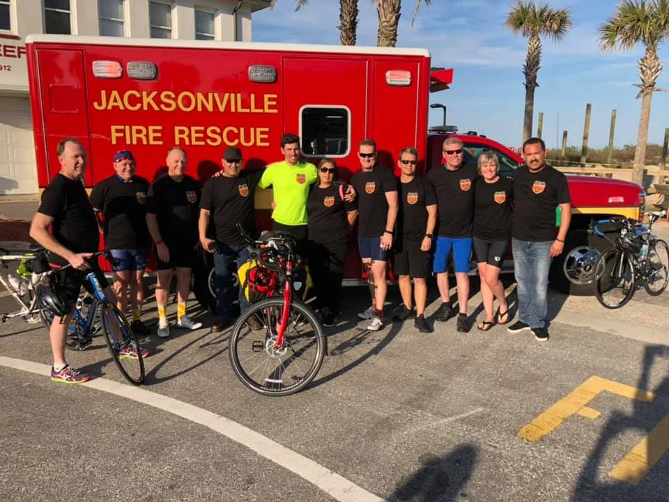 Cal fire/san diego county Fire apparatus engineer Thomas pitman in neon yellow shirt poses with Jacksonville beach firefighters at the end of his memorial bike ride.