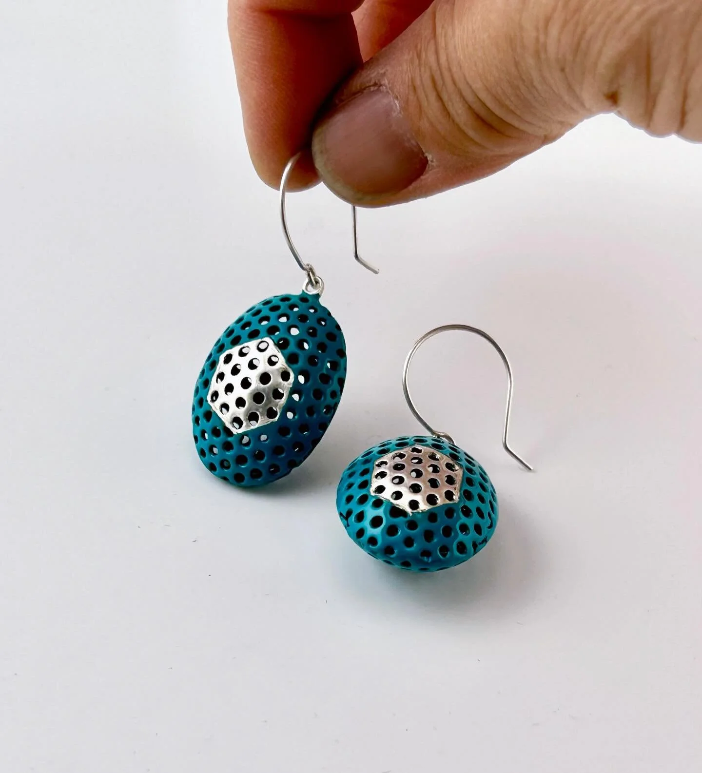 Oval domes in deep &lsquo;Deep Pool&rsquo; hues, with tiny hexagons infused along the geometric line and silver inlays at the back echoing the shape. Every detail is joined through the marriage-of-metal process, where metals meet and flow in quiet ha