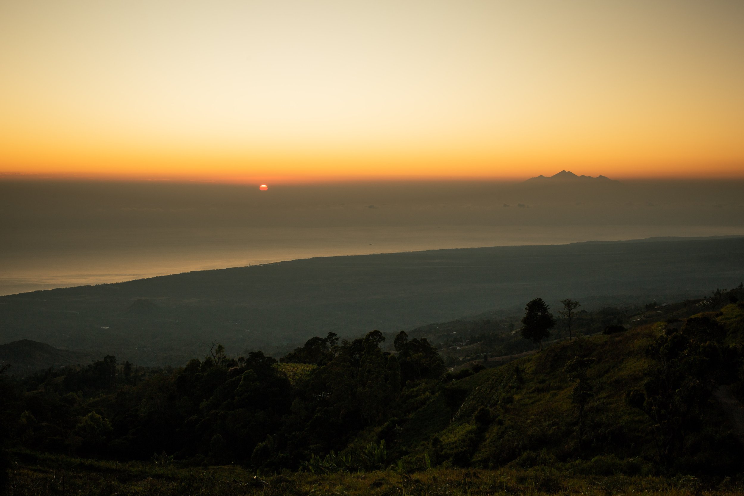 Sun rising over the sea on the left with Volcanoes of Lombok on the right