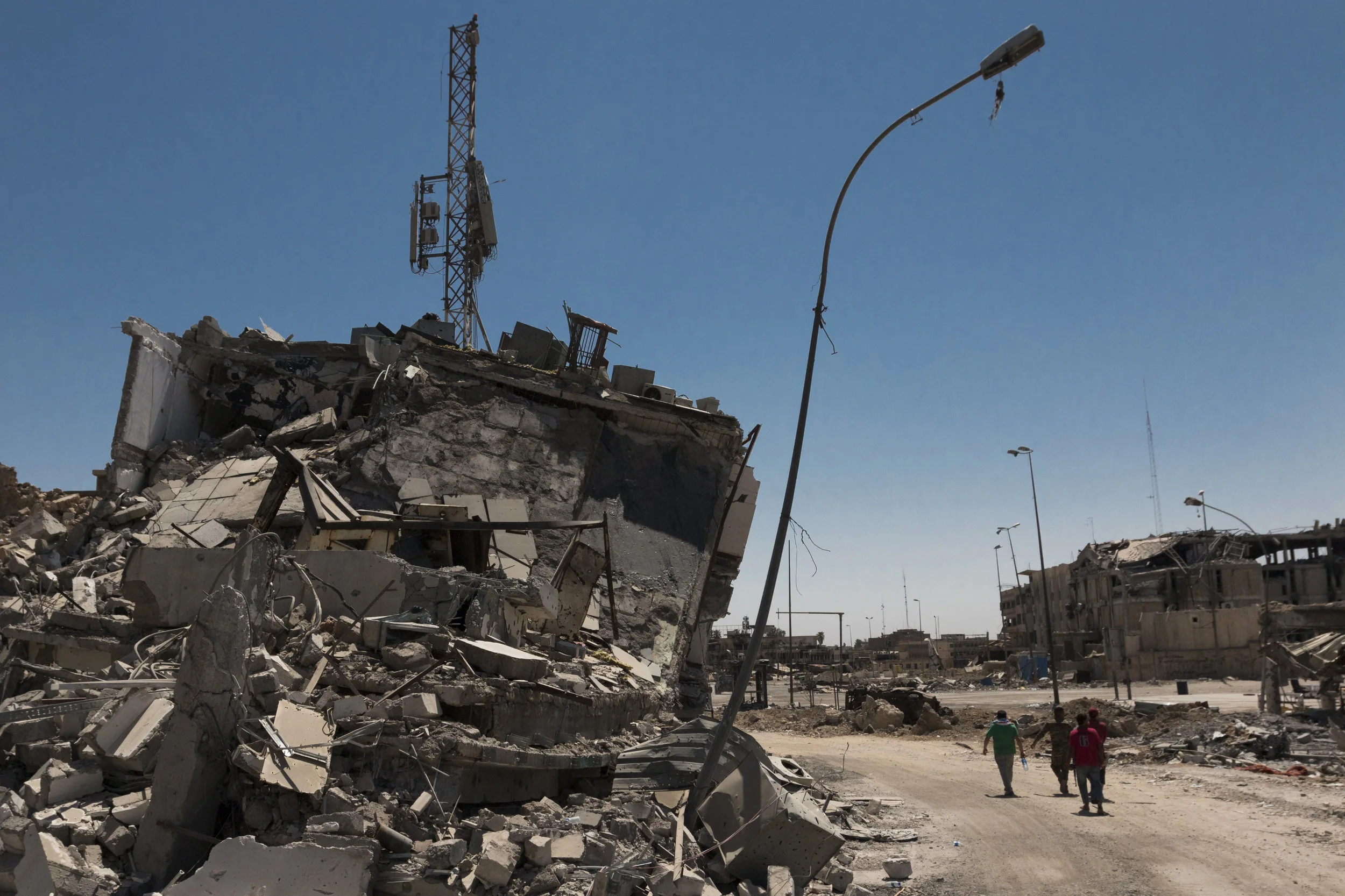 Civil defense force members and civilians walk through the destroyed ruins of West Mosul in order to recover the remains of two individuals in the Old City