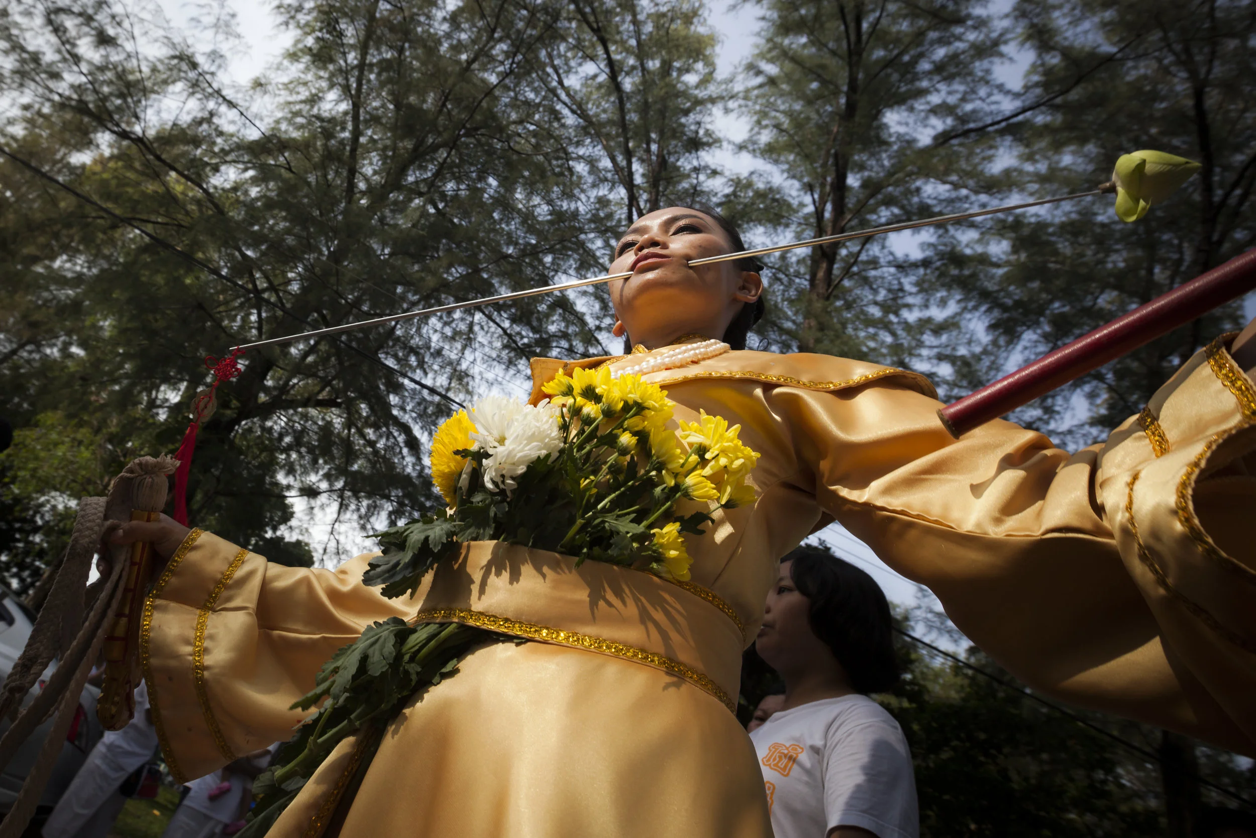 A female mah song devotee walks with a long metal piercing through her cheek while holding a ceremonial whip and rod October 13, 2018.