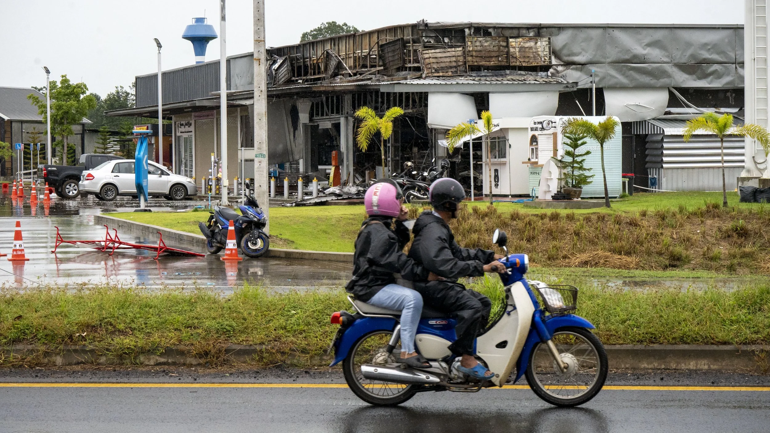 On July 27th, 2025 local residents ride their motor scooter past the bombed and burned out 7-11 convenience store in Ban Phue, Sisaket province which was hit by Cambodian munitions. At least 6 people, including 2 school children, were killed and sev