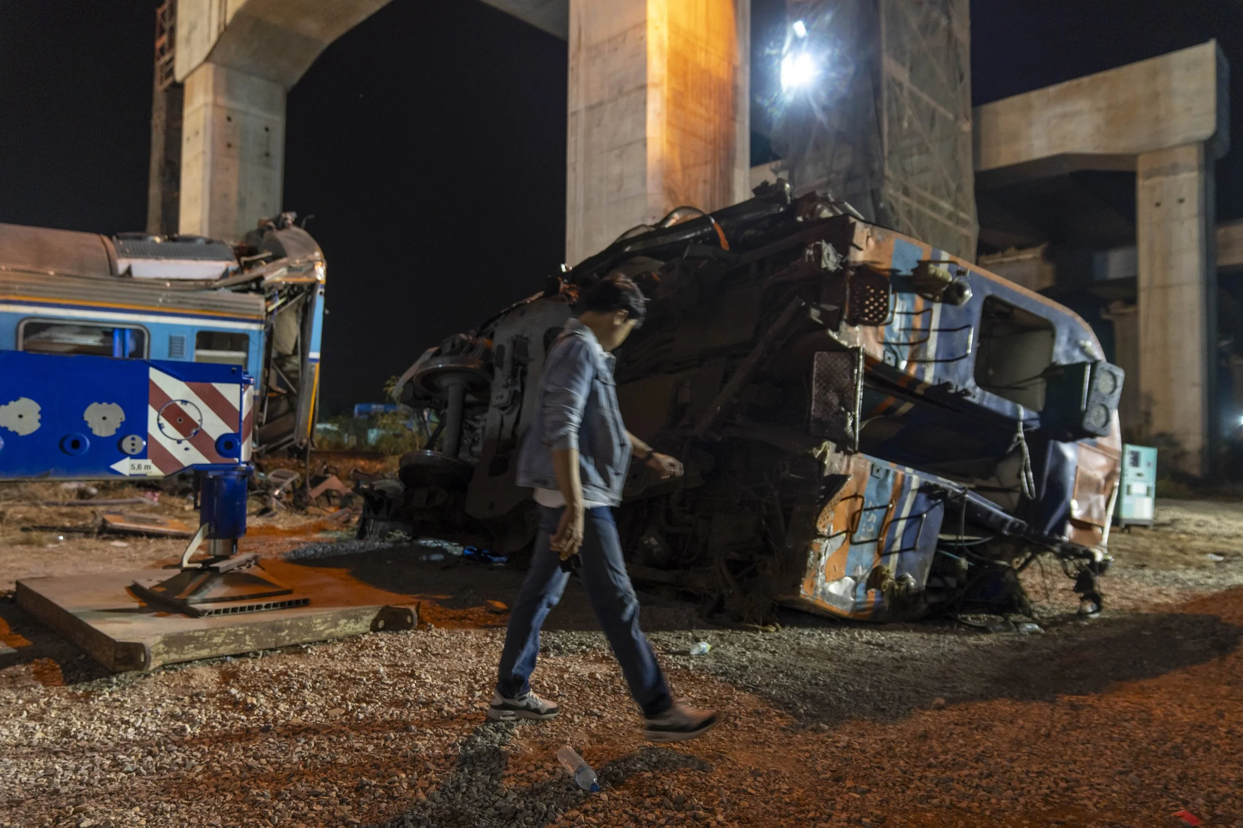  January 14, 2026: A man walks past a train car which was derailed by a falling crane while the train was was moving underneath the Thai-Chinese high speed rail construction site, approximately 12 hours after the disaster which claimed 32 lives - for