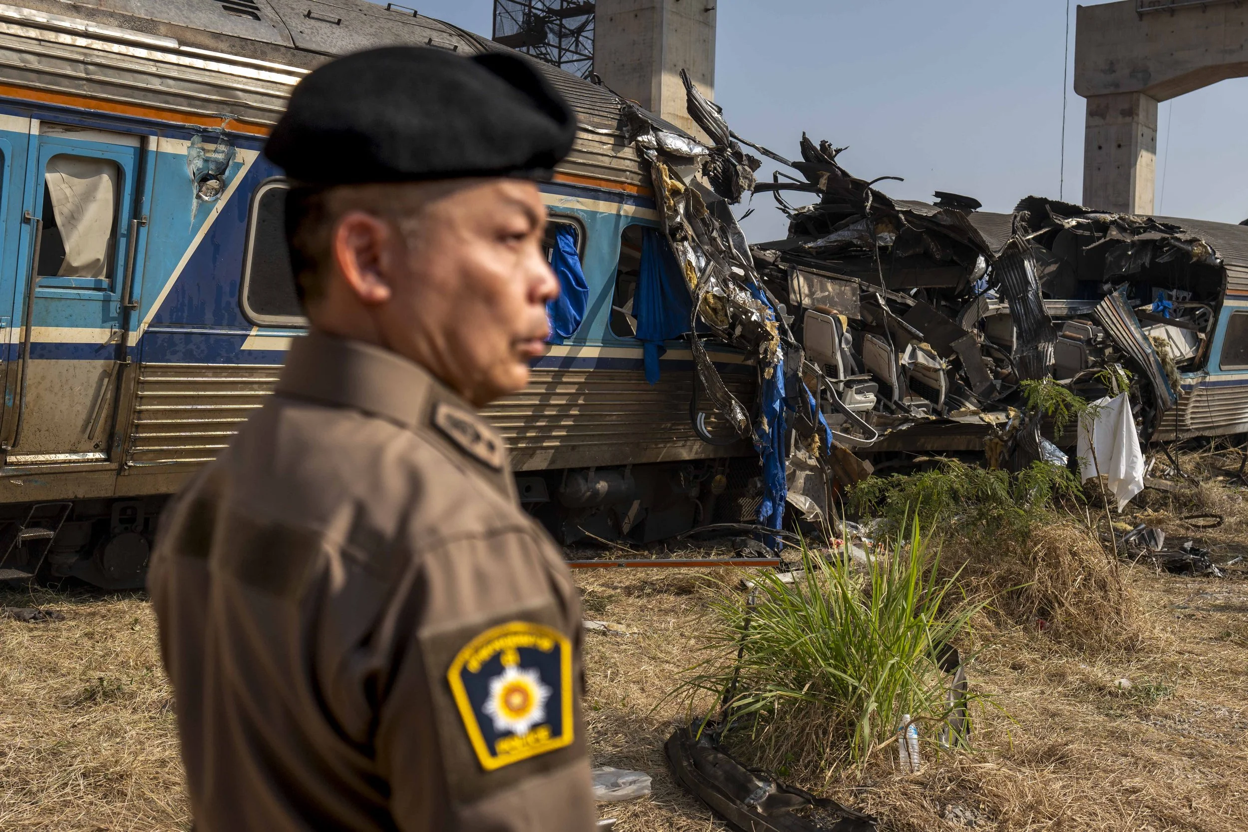  January 15, 2026: A police officer stands near a heavily damaged train car the morning after it was crushed by a falling crane while the train was was moving underneath the Thai-Chinese high speed rail construction site and resulted in 32 deaths - f