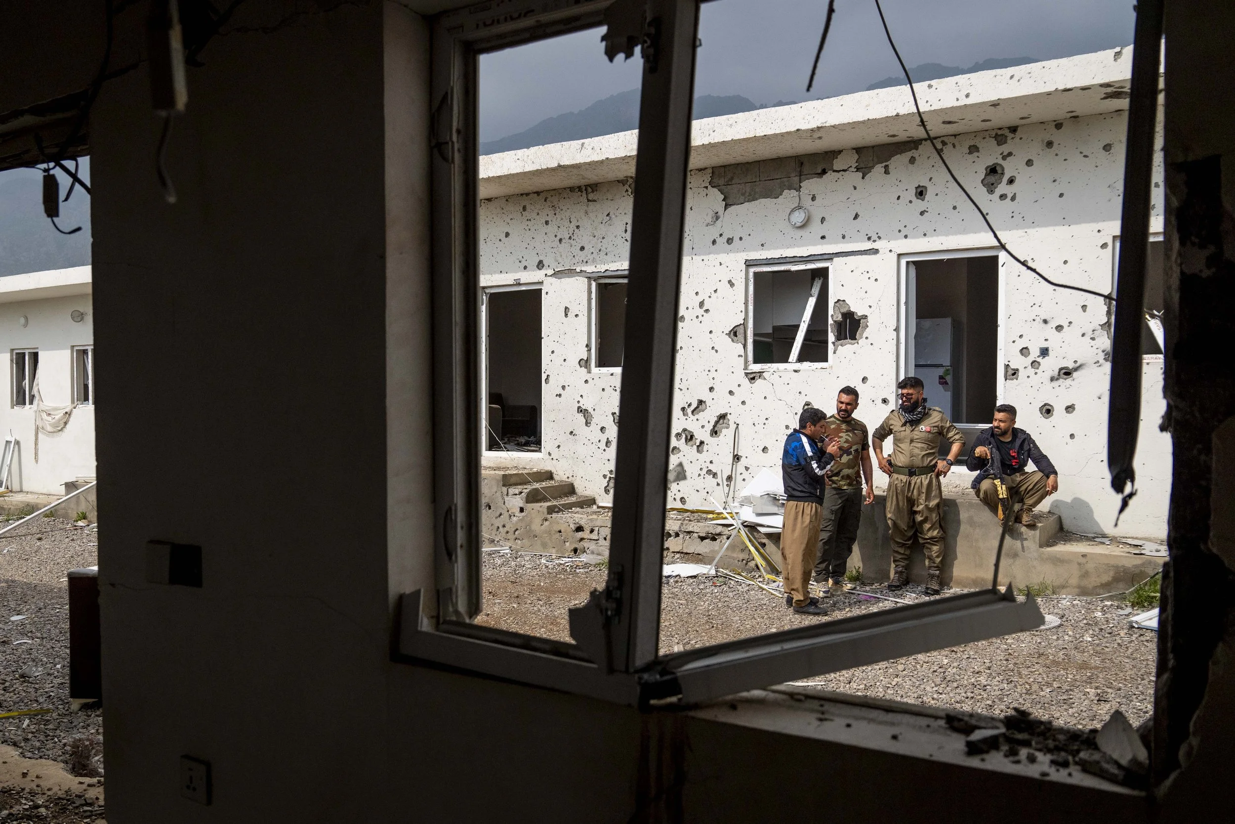  4 Komala members stand and talk neat the shrapnel scared buildings of their Surdash camp. 