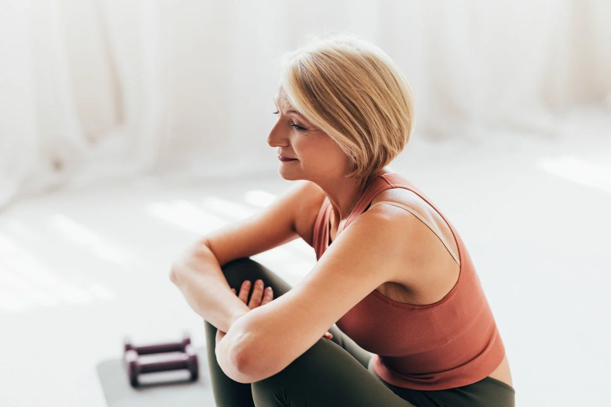 Woman over 40 sitting thoughtfully after a workout, reflecting on why her fitness routine is not working