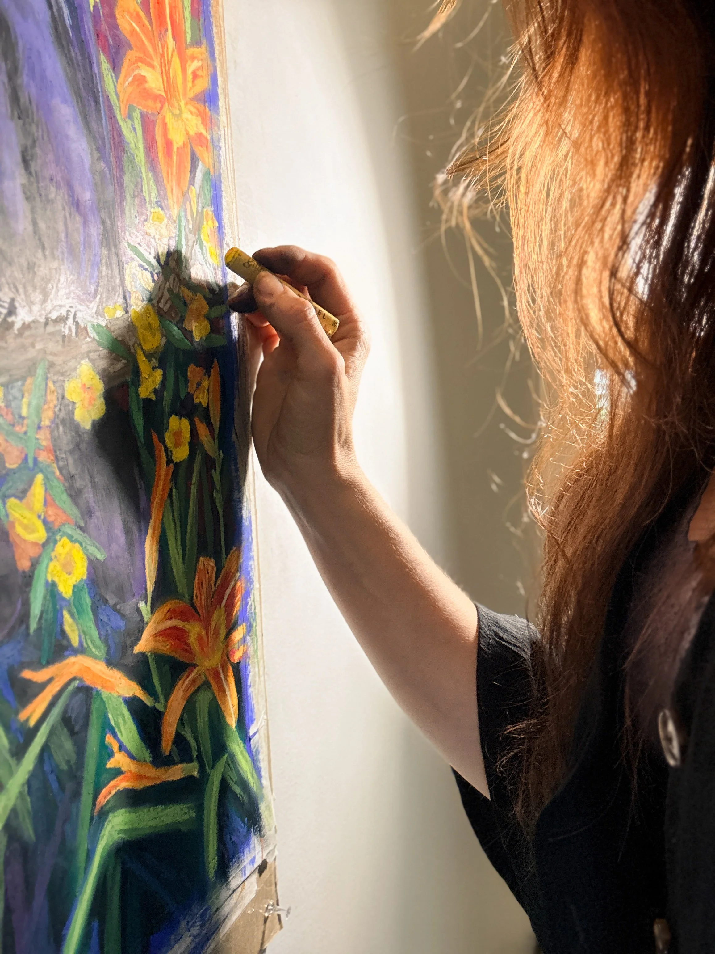 A woman with long red hair is painting a colorful floral scene on a canvas with bright orange, yellow, purple, and green flowers.