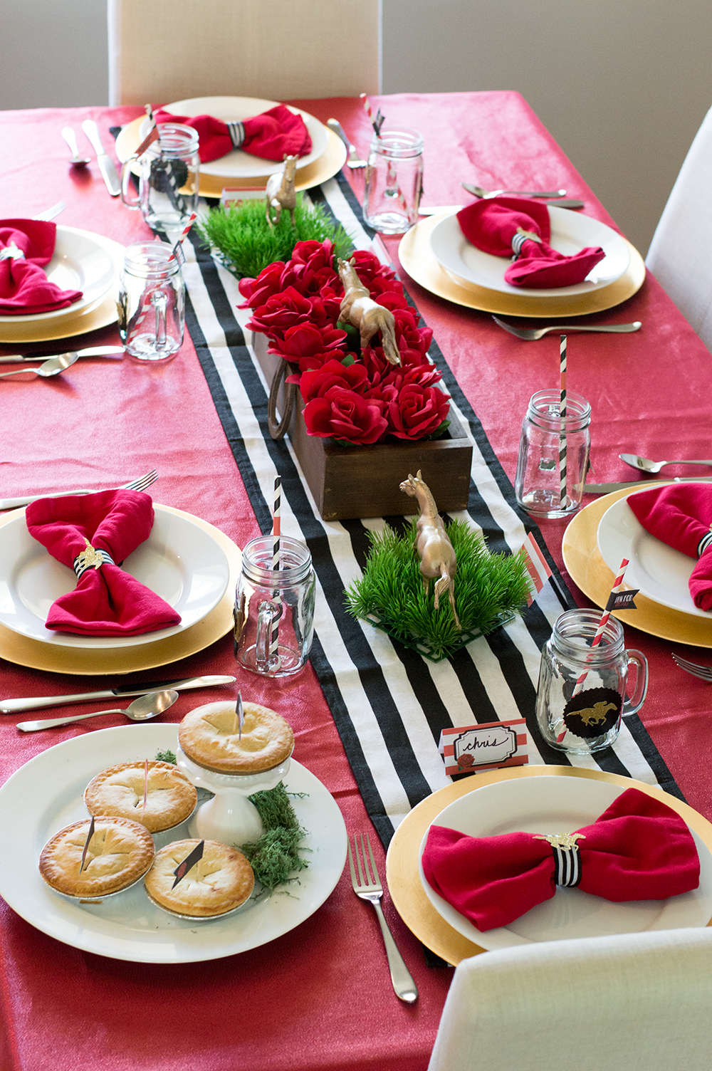  Red tablecloth with black and white striped runner and a rose centerpiece make the perfect Kentucky Derby dinner party setting. 