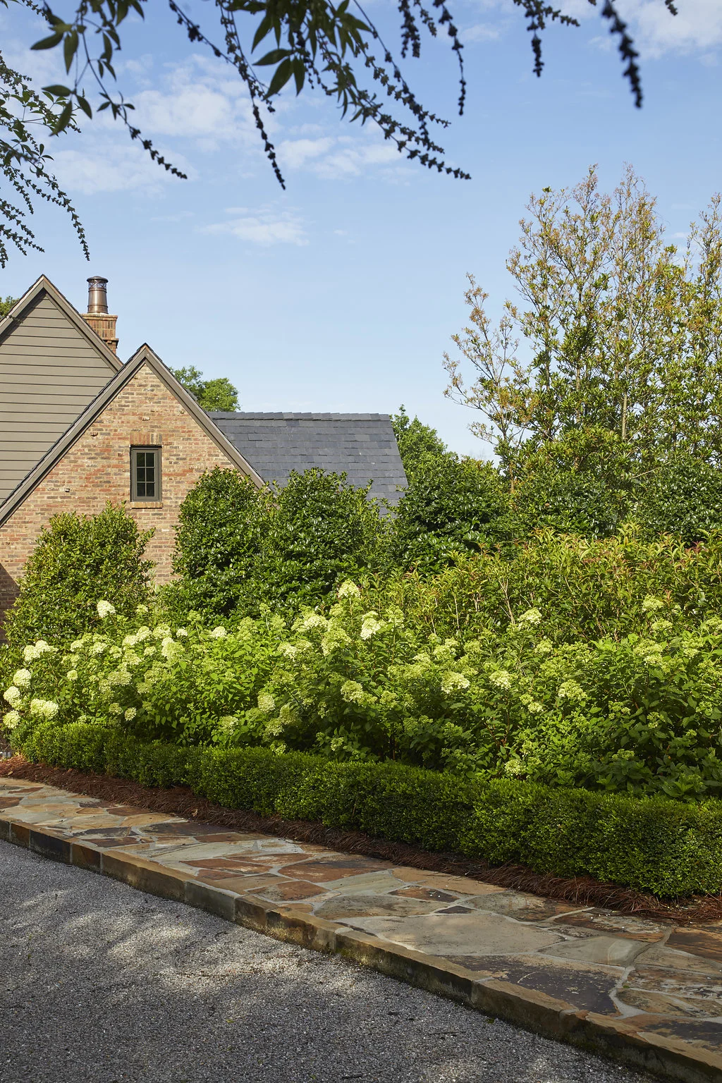 Flower bushes and shrubbery lining the driveway.